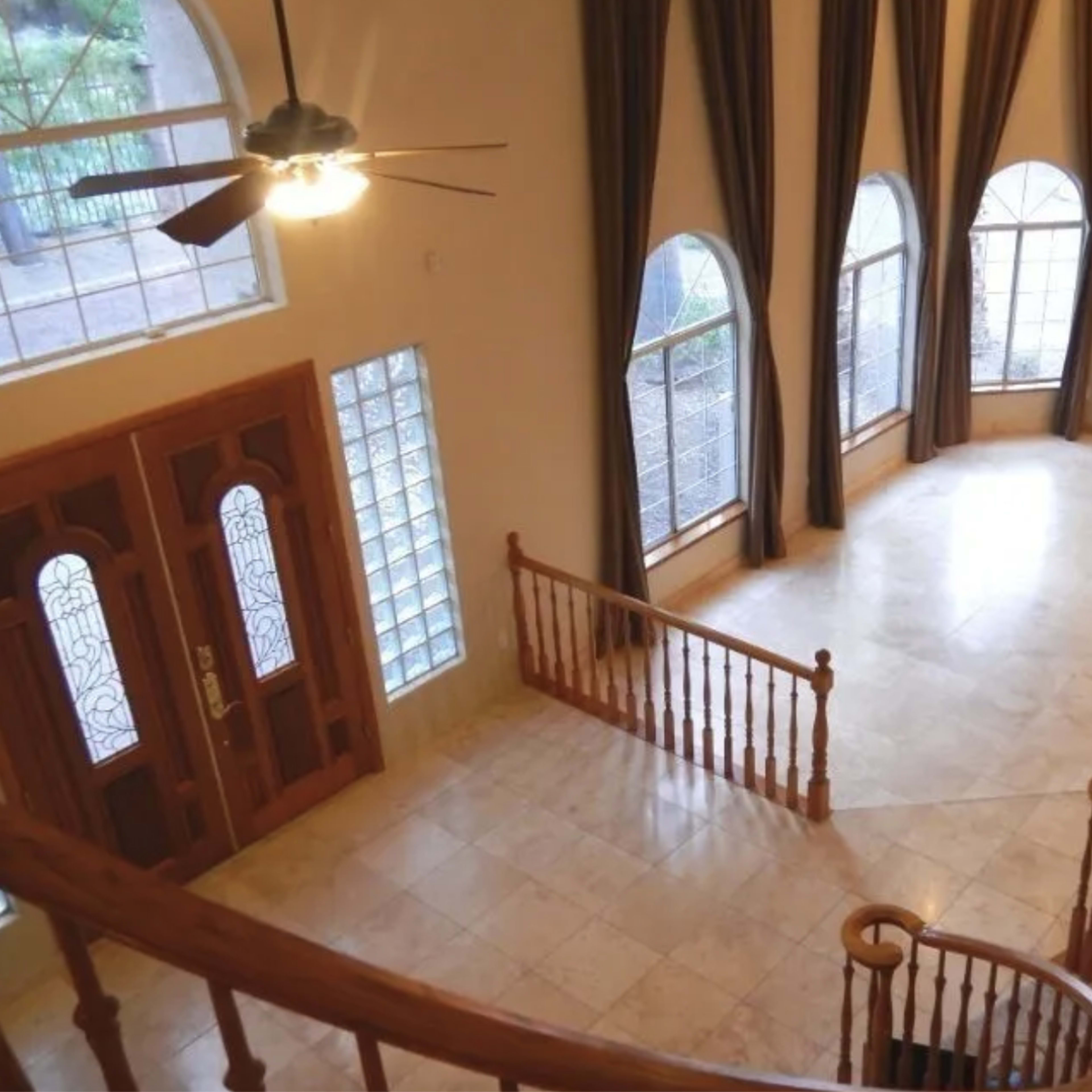 A spacious, empty living area with large arched windows, a stone fireplace, and a curved staircase.