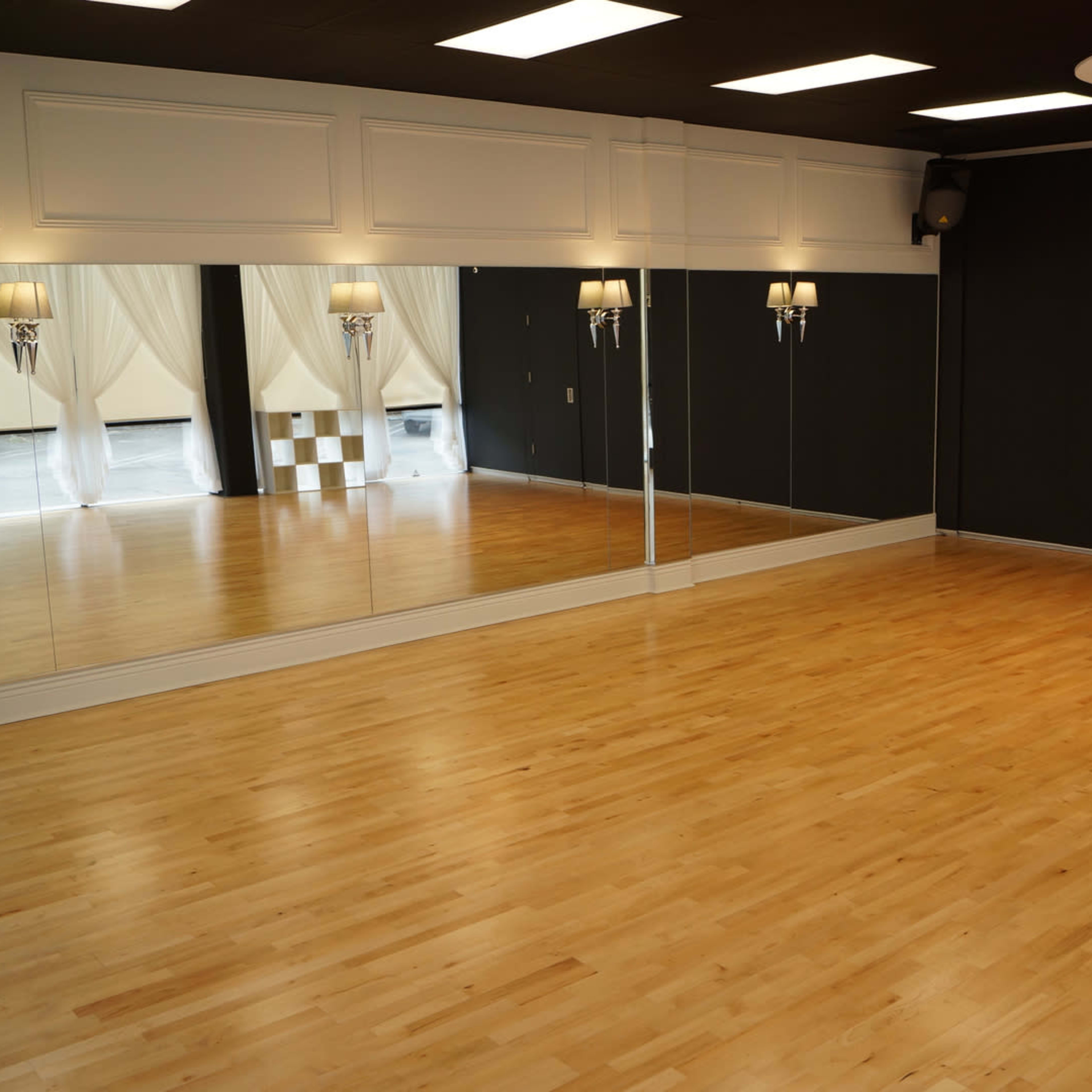 A spacious dance studio with wooden flooring, large mirrors, and elegant lighting fixtures.