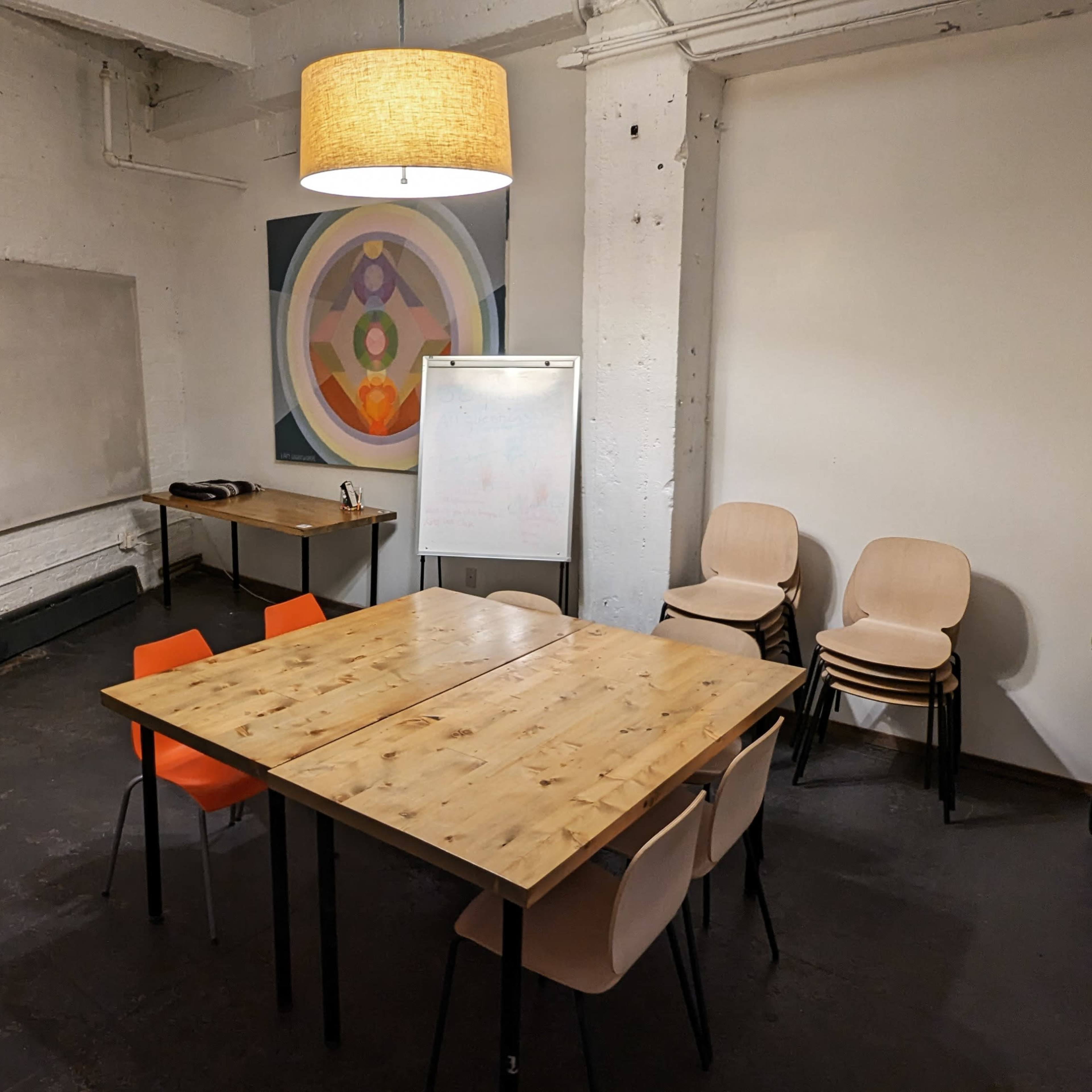 A meeting room featuring a wooden table surrounded by chairs, a whiteboard, and a lamp hanging from the ceiling.