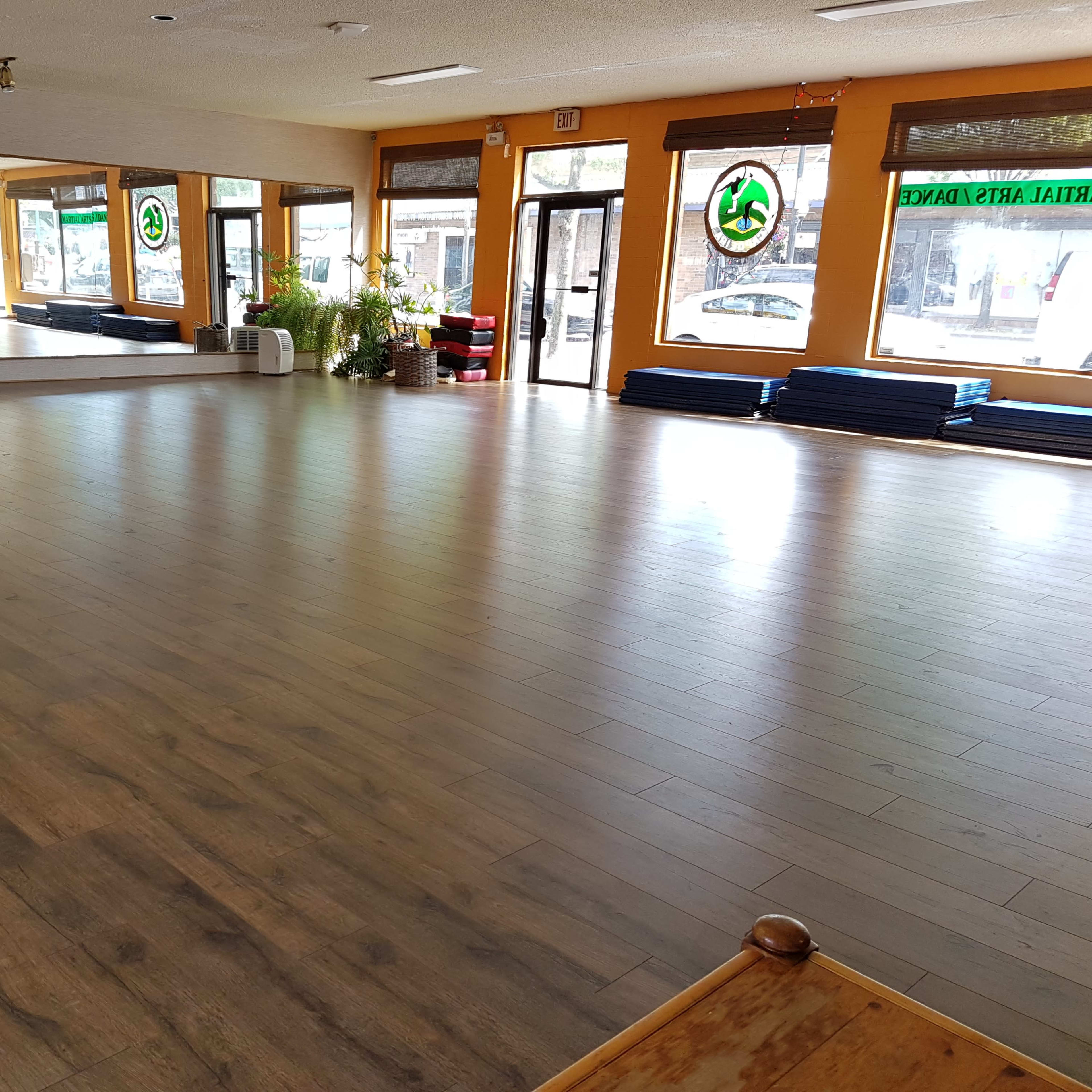 A spacious dance studio with wooden floors, large windows, and mirrors along one wall.