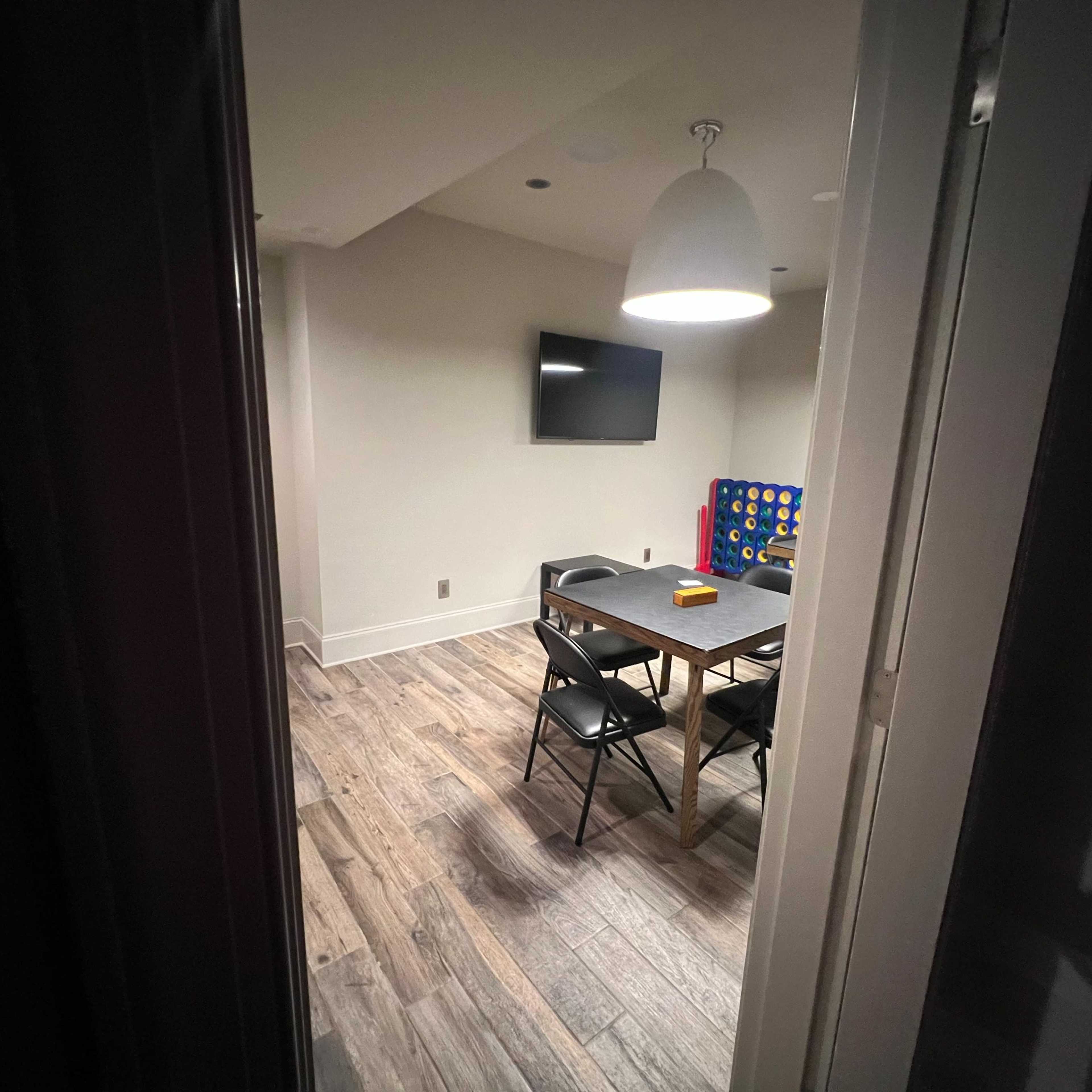 A view into a room featuring a table and chairs, a television on the wall, and a game set against one side.