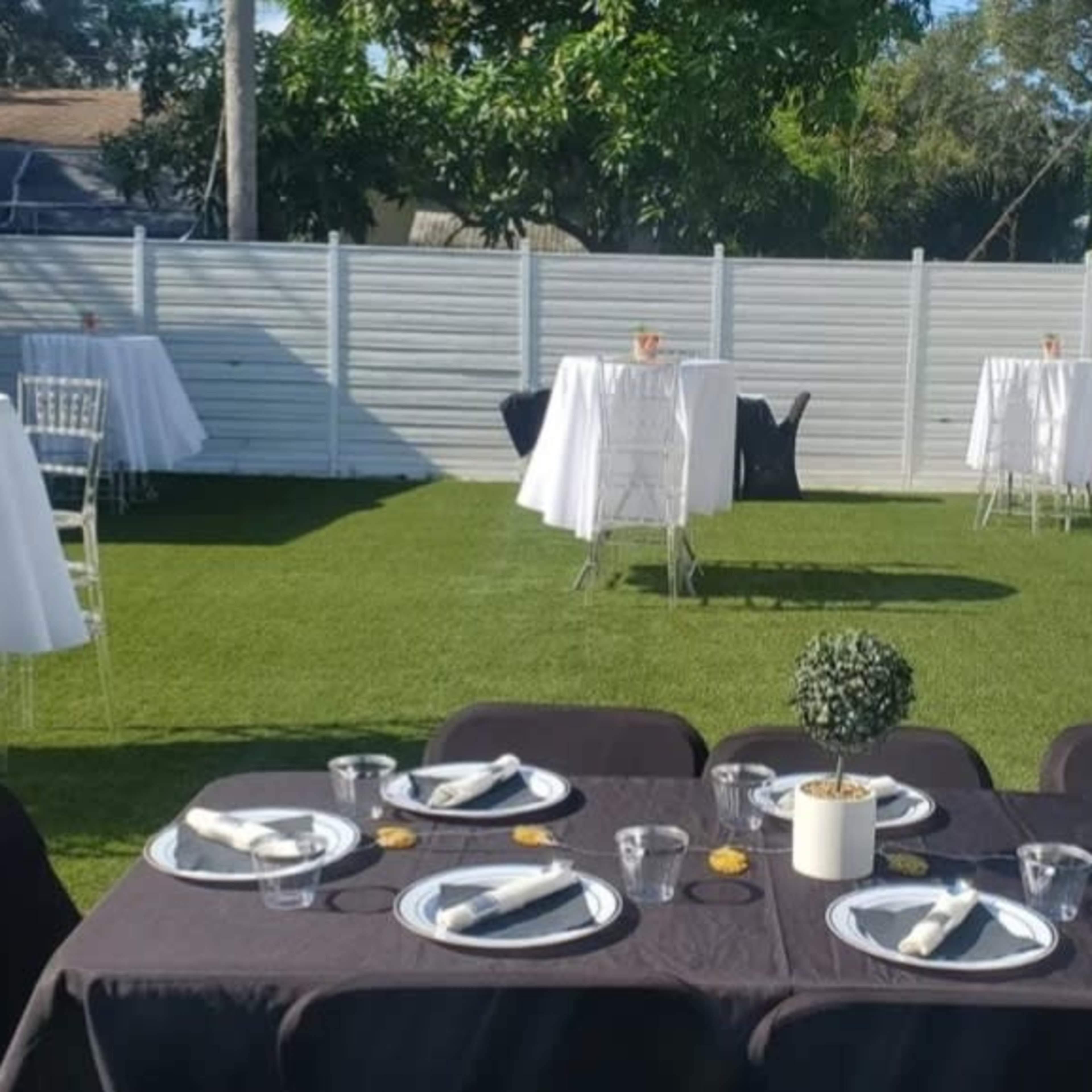 A backyard event setup featuring several decorated tables and chairs arranged on a lawn.