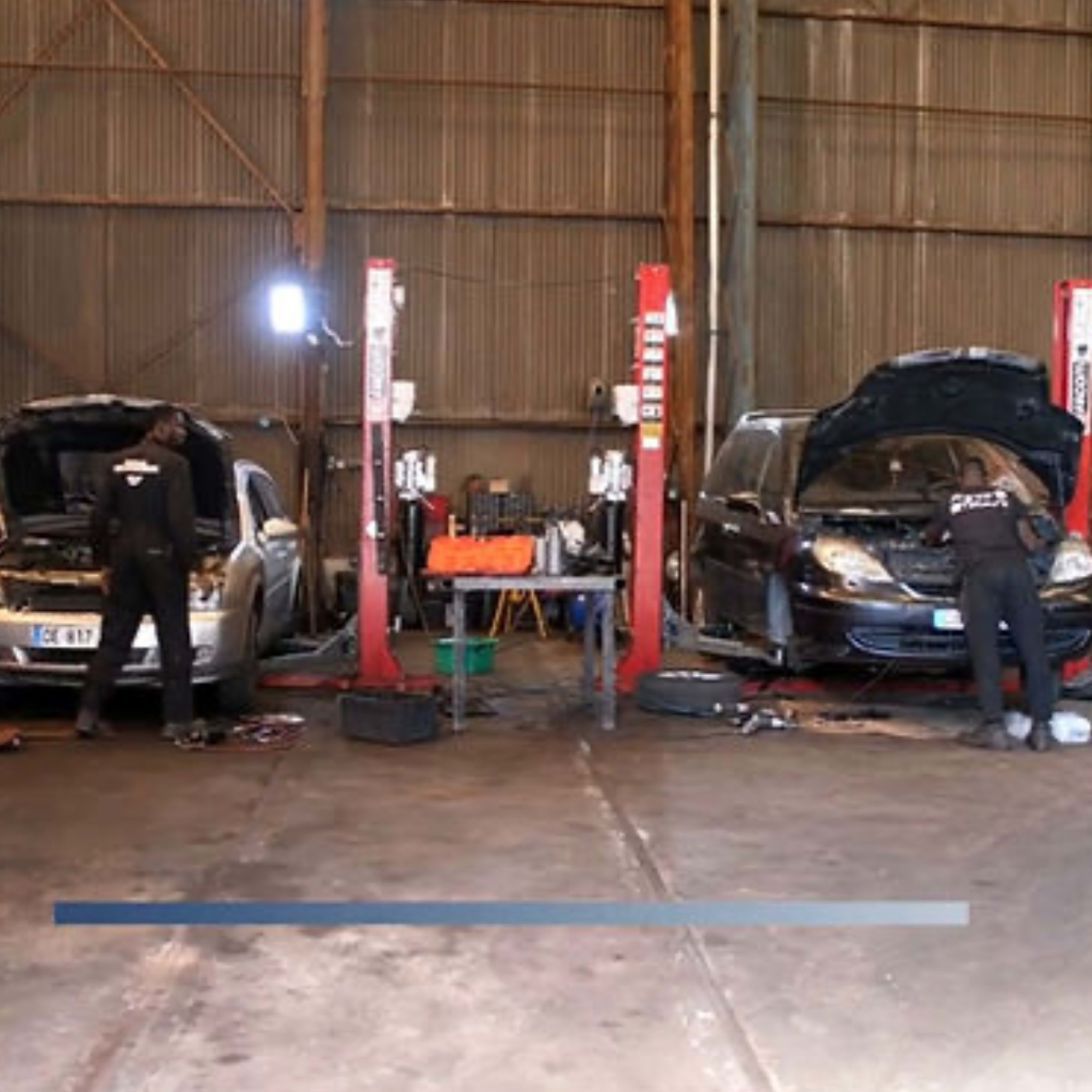 Two mechanics work on cars positioned on hydraulic lifts in an automotive repair shop.