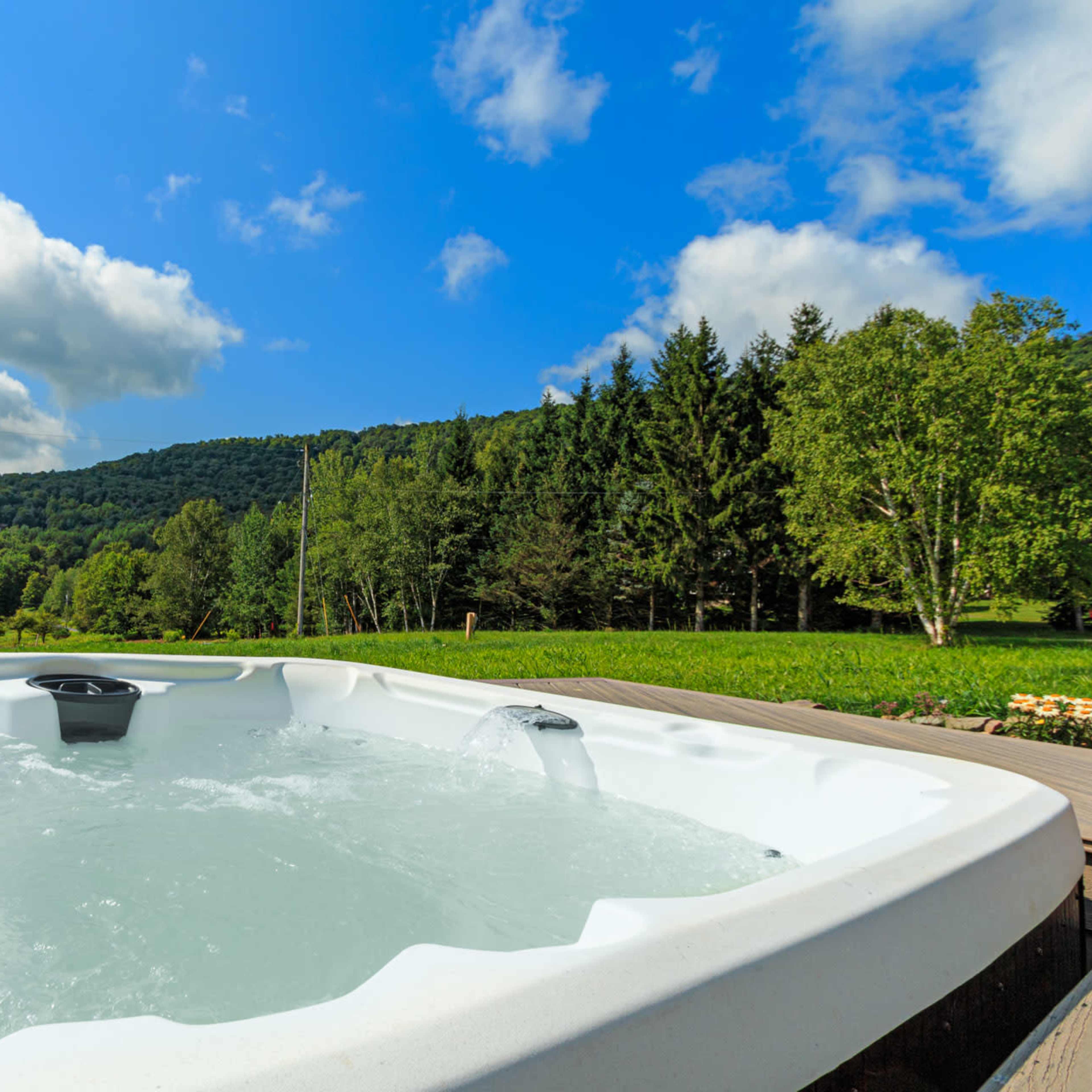 A hot tub sits on a wooden deck overlooking a lush green landscape under a partly cloudy sky.