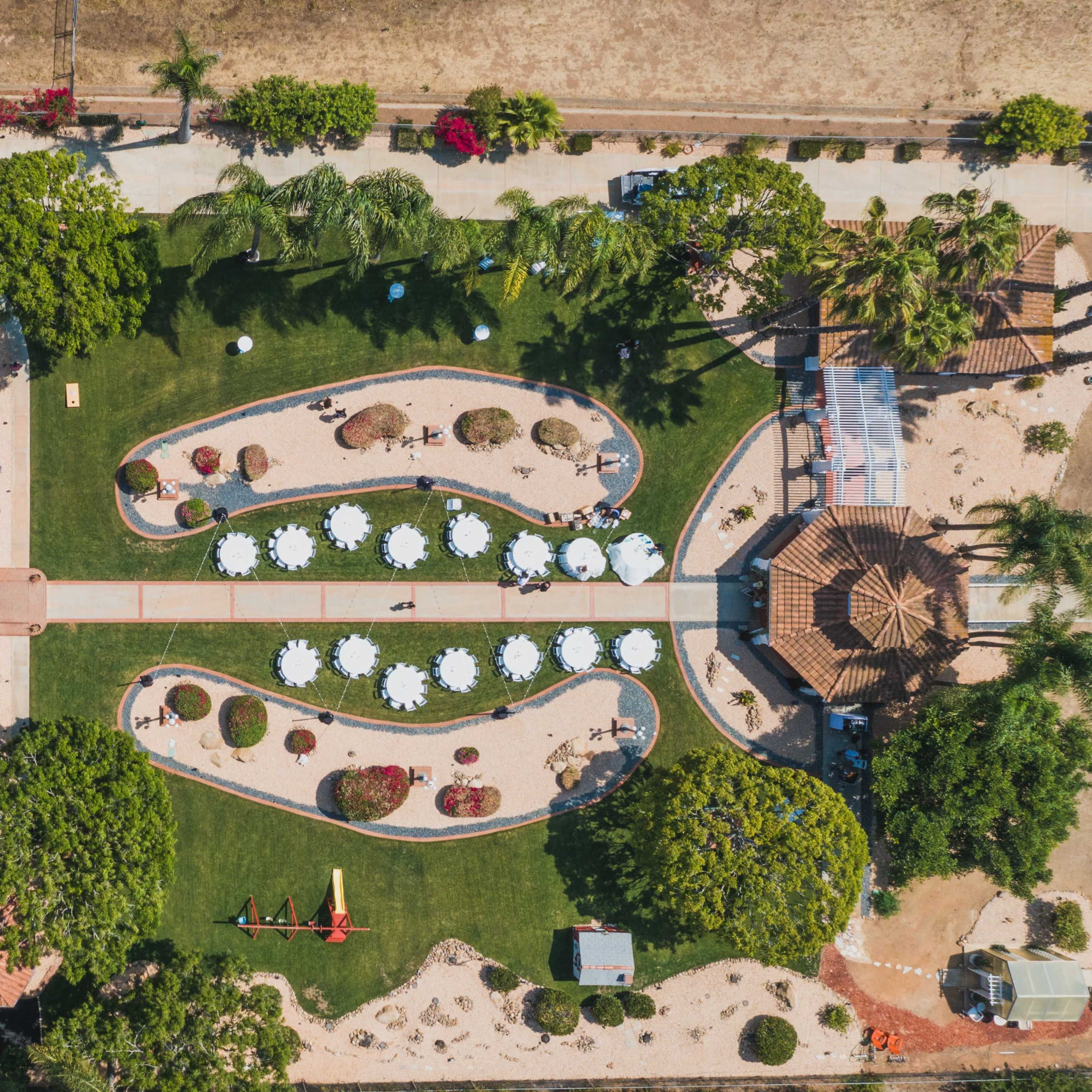 An aerial view shows a landscaped property with a main building, parking area, garden paths, seating arrangements, and a gazebo surrounded by greenery.
