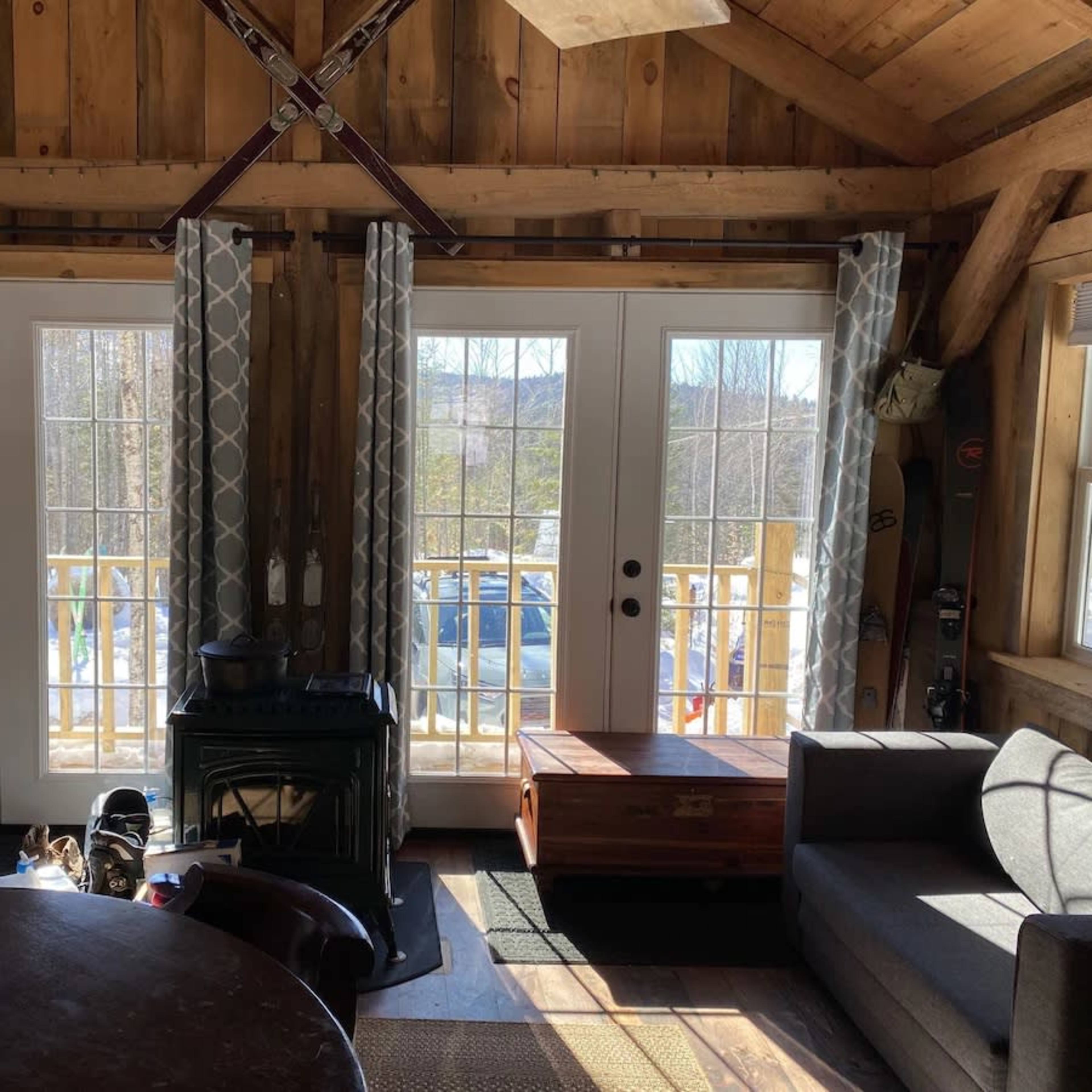 A cozy cabin interior featuring two sets of double doors leading to a deck, with a circular dining table and a couch nearby.