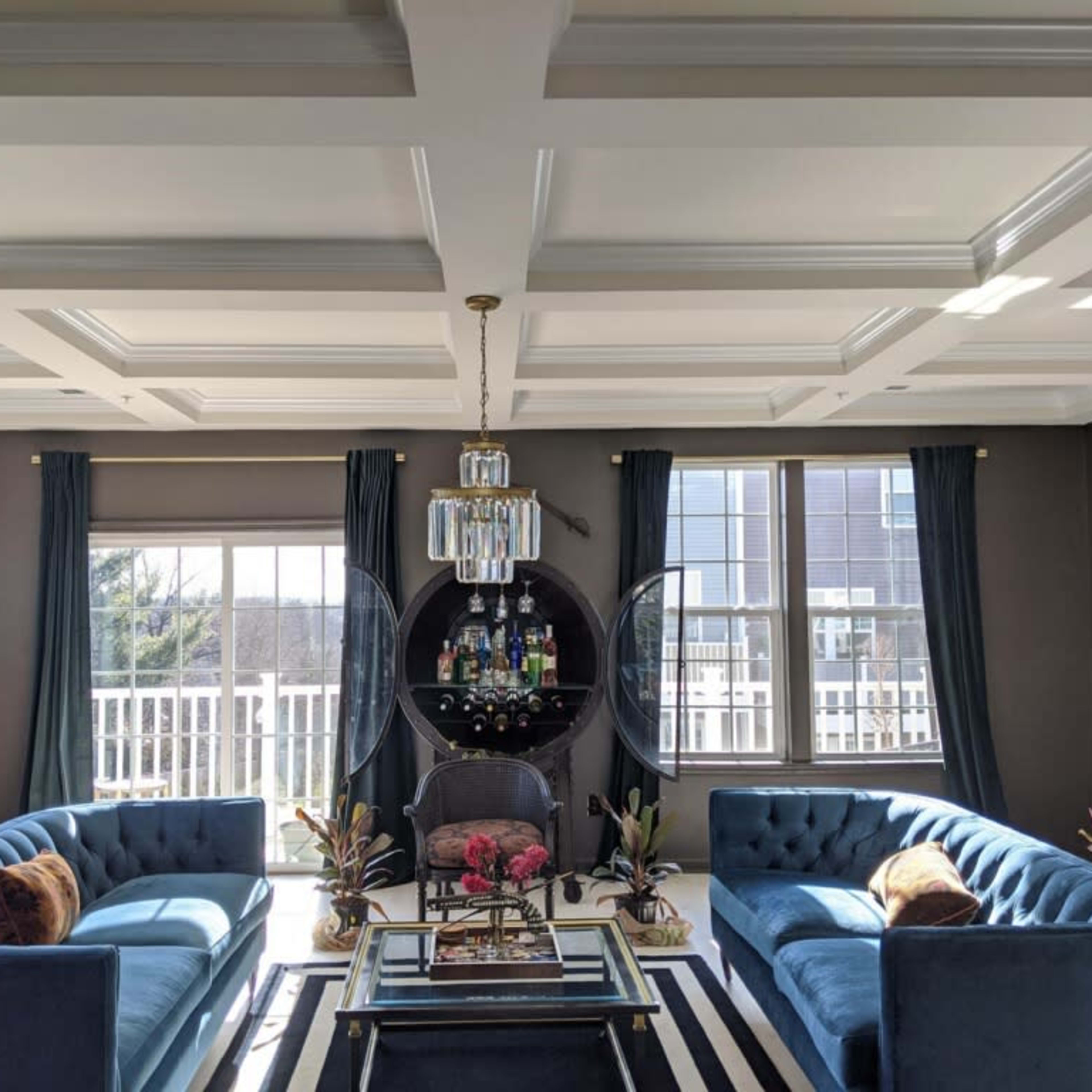 A modern living room featuring two blue sofas facing each other, a glass coffee table with a decorative arrangement, and large windows with sheer curtains.