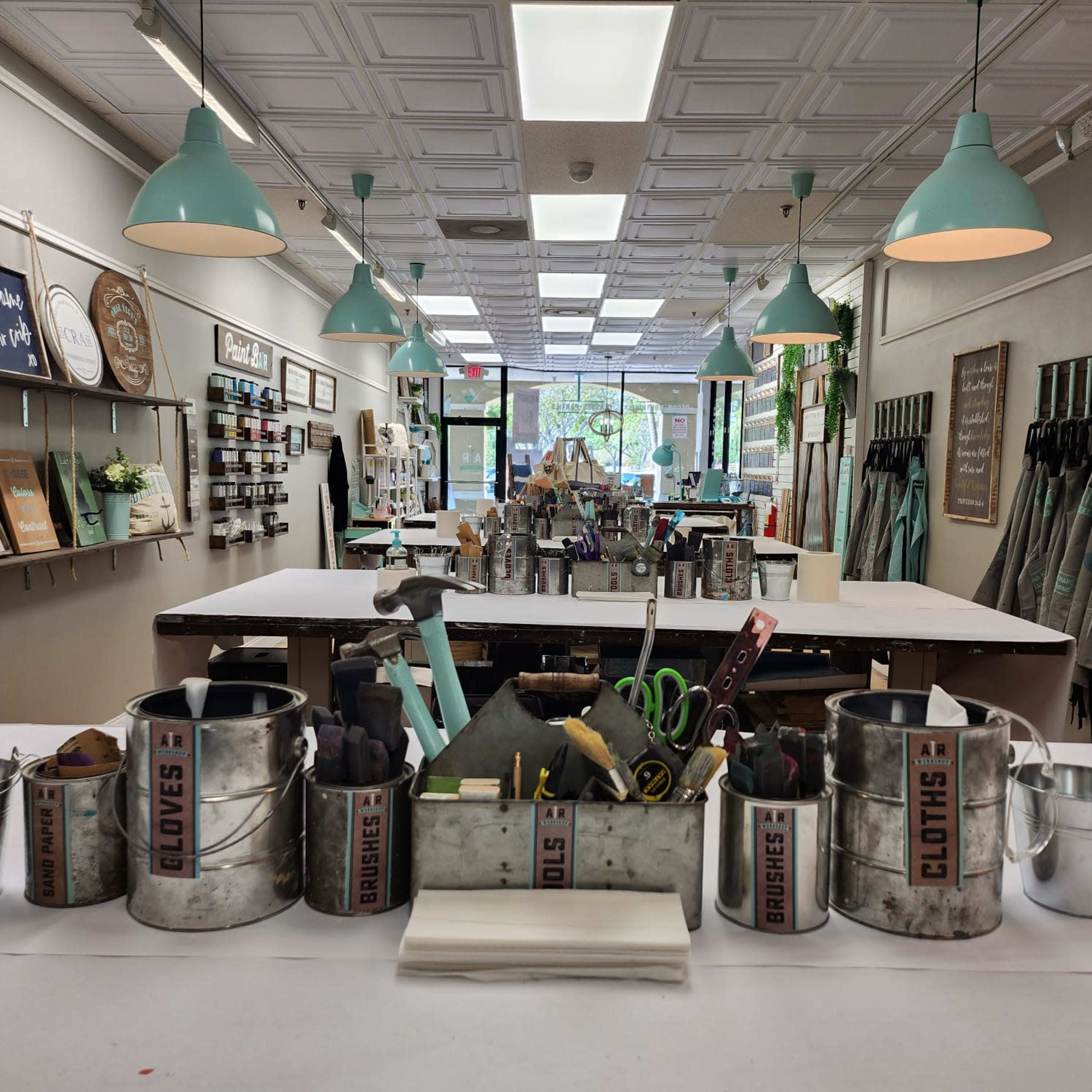 A craft studio with a central table filled with various tools and supplies, surrounded by decorated walls and organized workspaces.