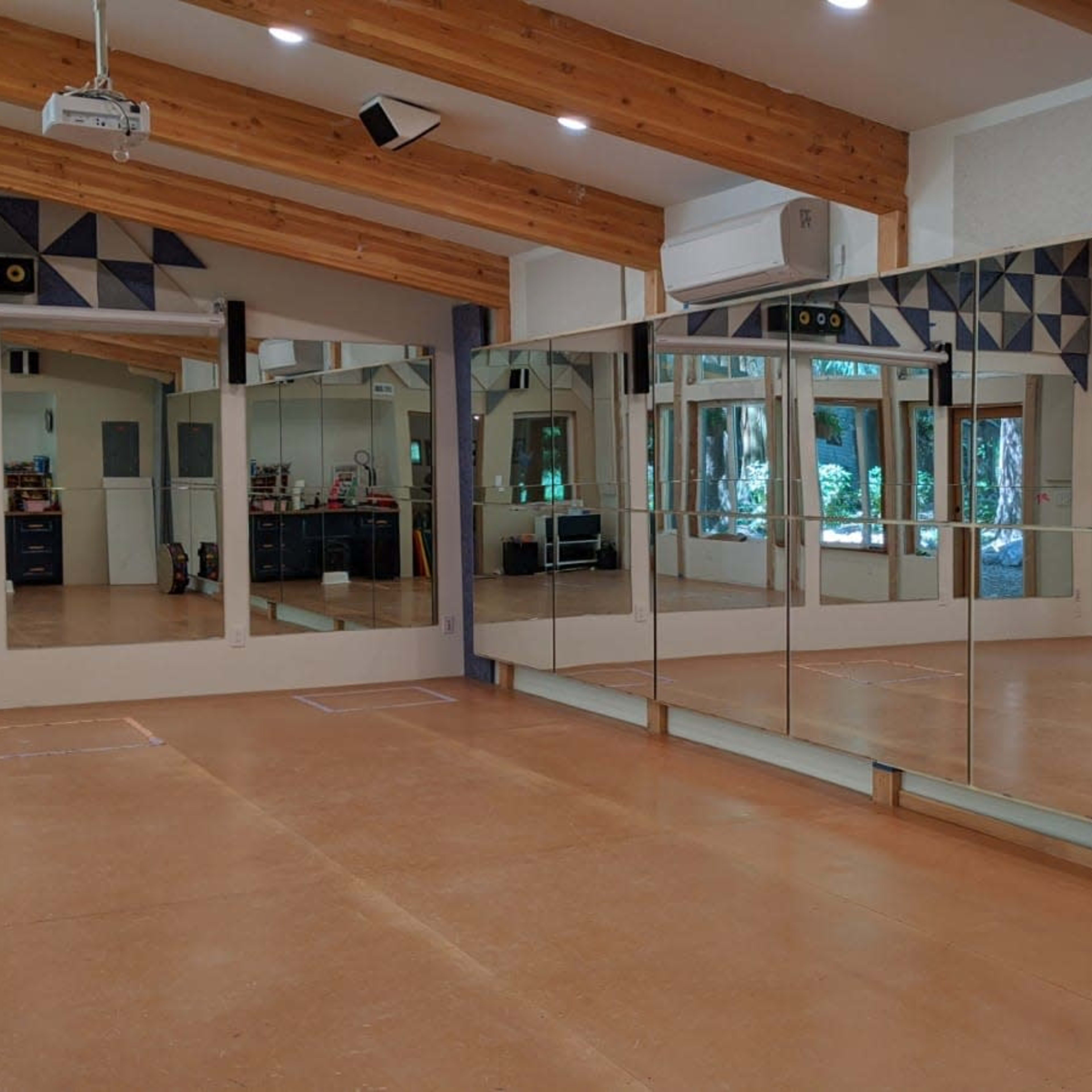 A spacious room with large mirrors on one wall, wooden beams on the ceiling, and windows letting in natural light.