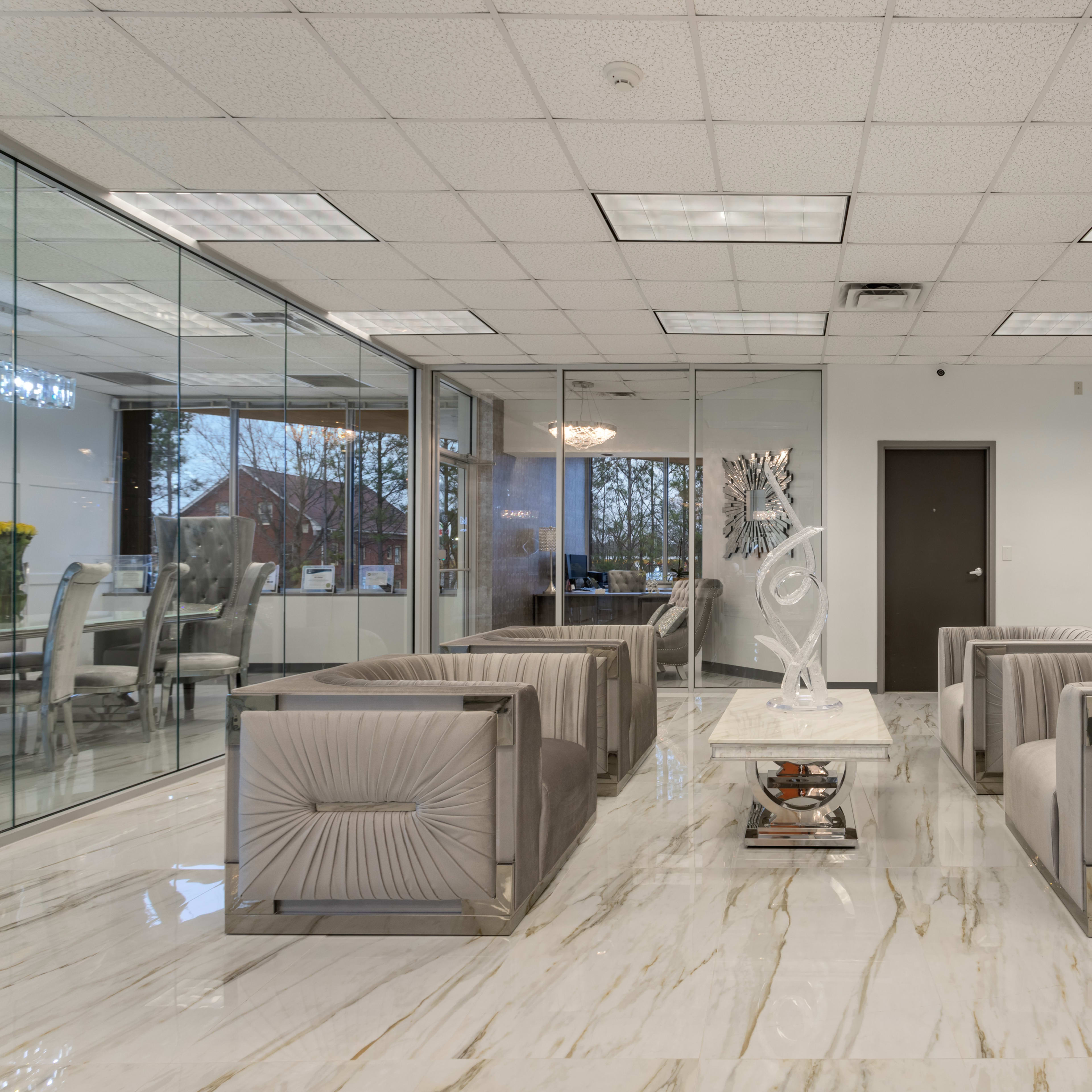 A modern reception area with marble flooring, gray seating, and a glass-walled meeting room in the background.
