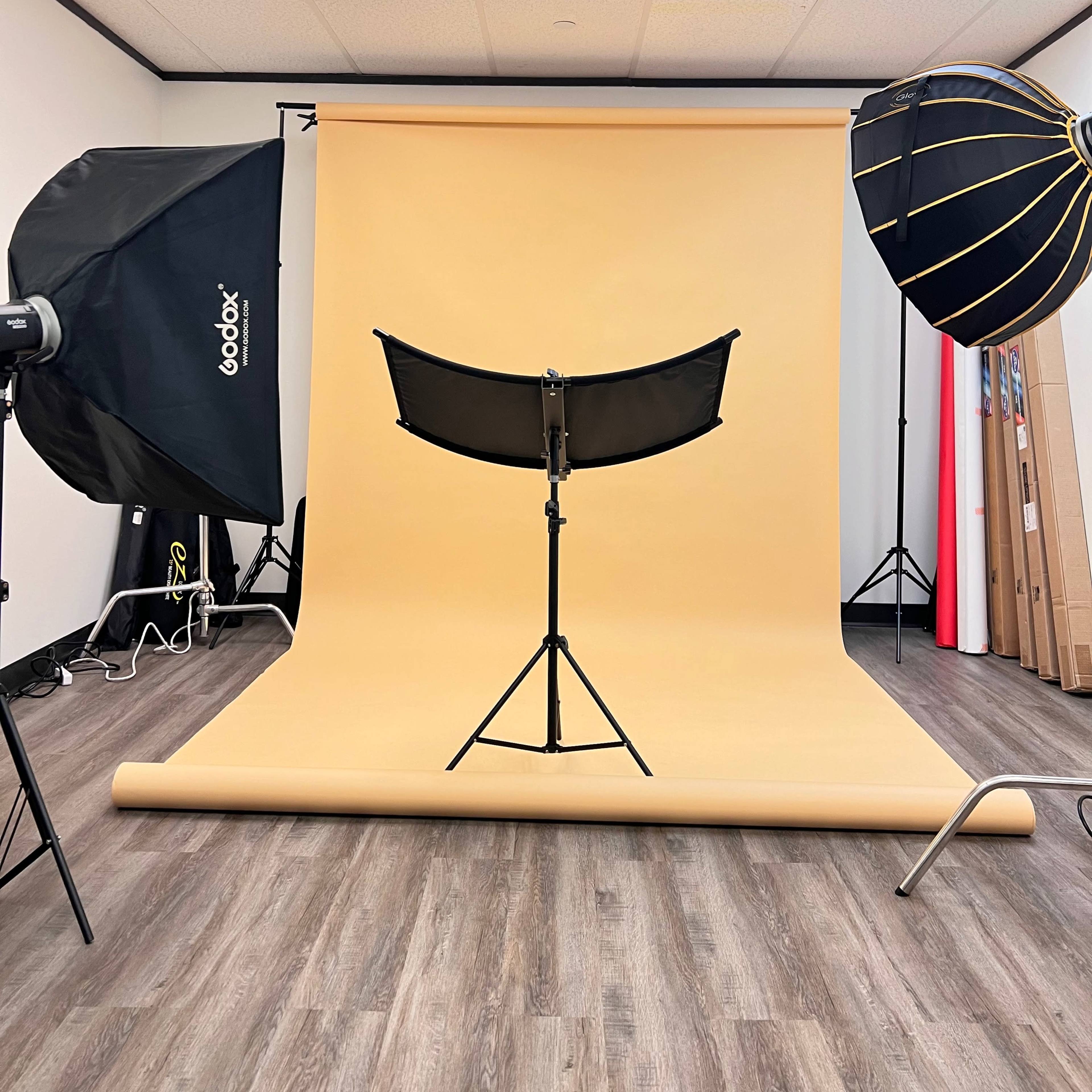 A photography studio features a yellow backdrop, lighting equipment, and a stand positioned in the center.