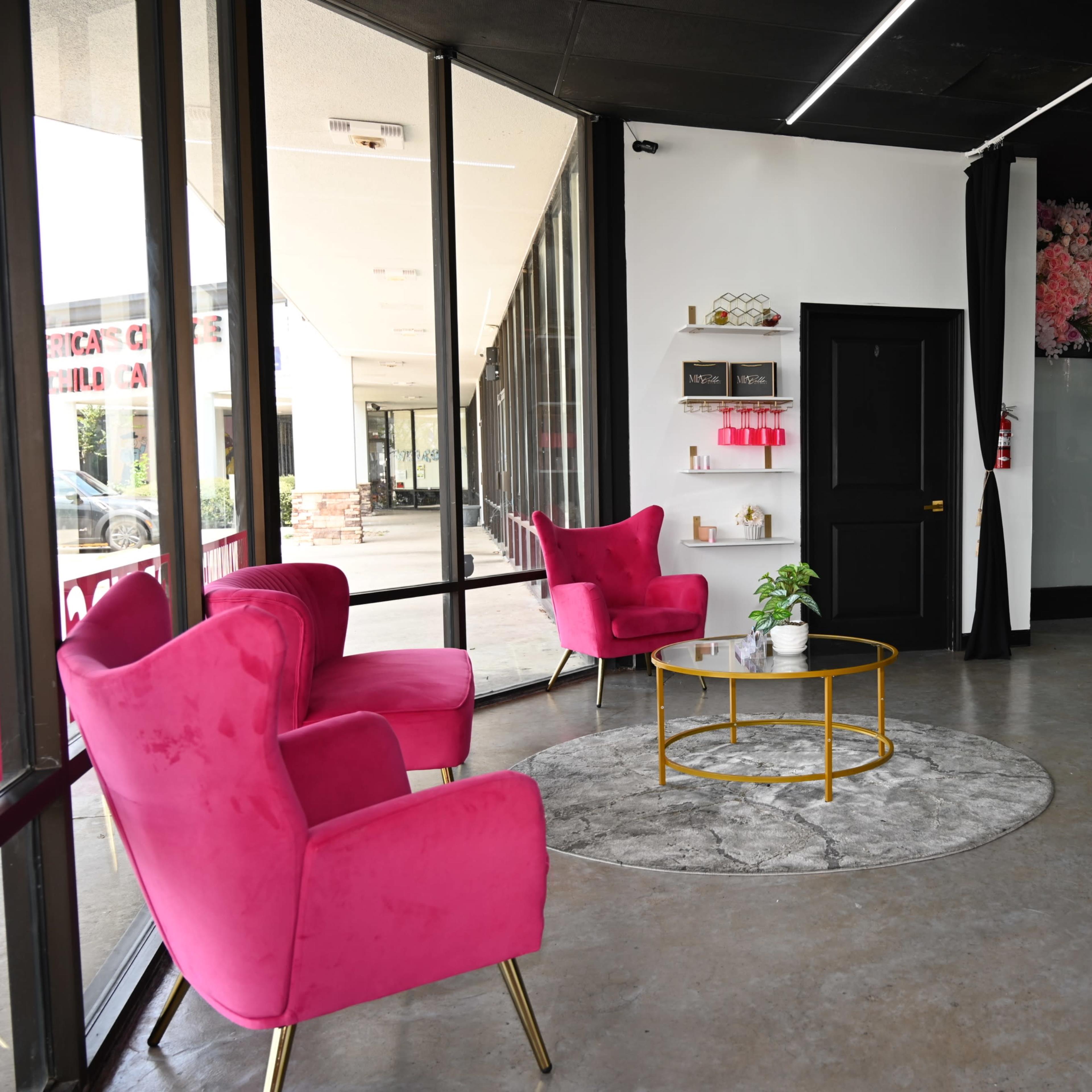 A modern interior features two pink armchairs, a round gold coffee table, and a decorative wall with floral designs.