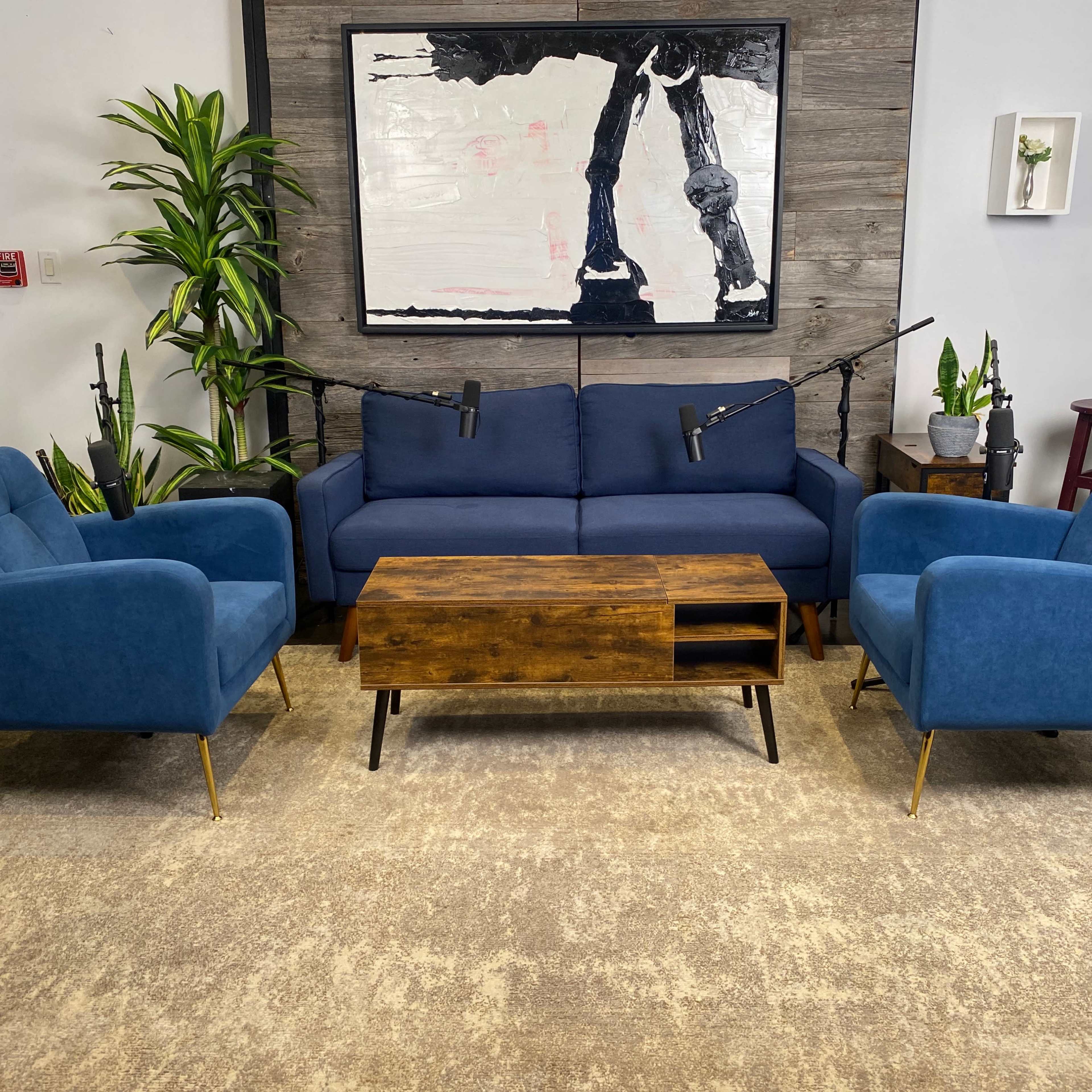 A modern, minimalist living room setup with a blue sofa, two matching armchairs, a wooden coffee table, and decorative plants against a neutral background.