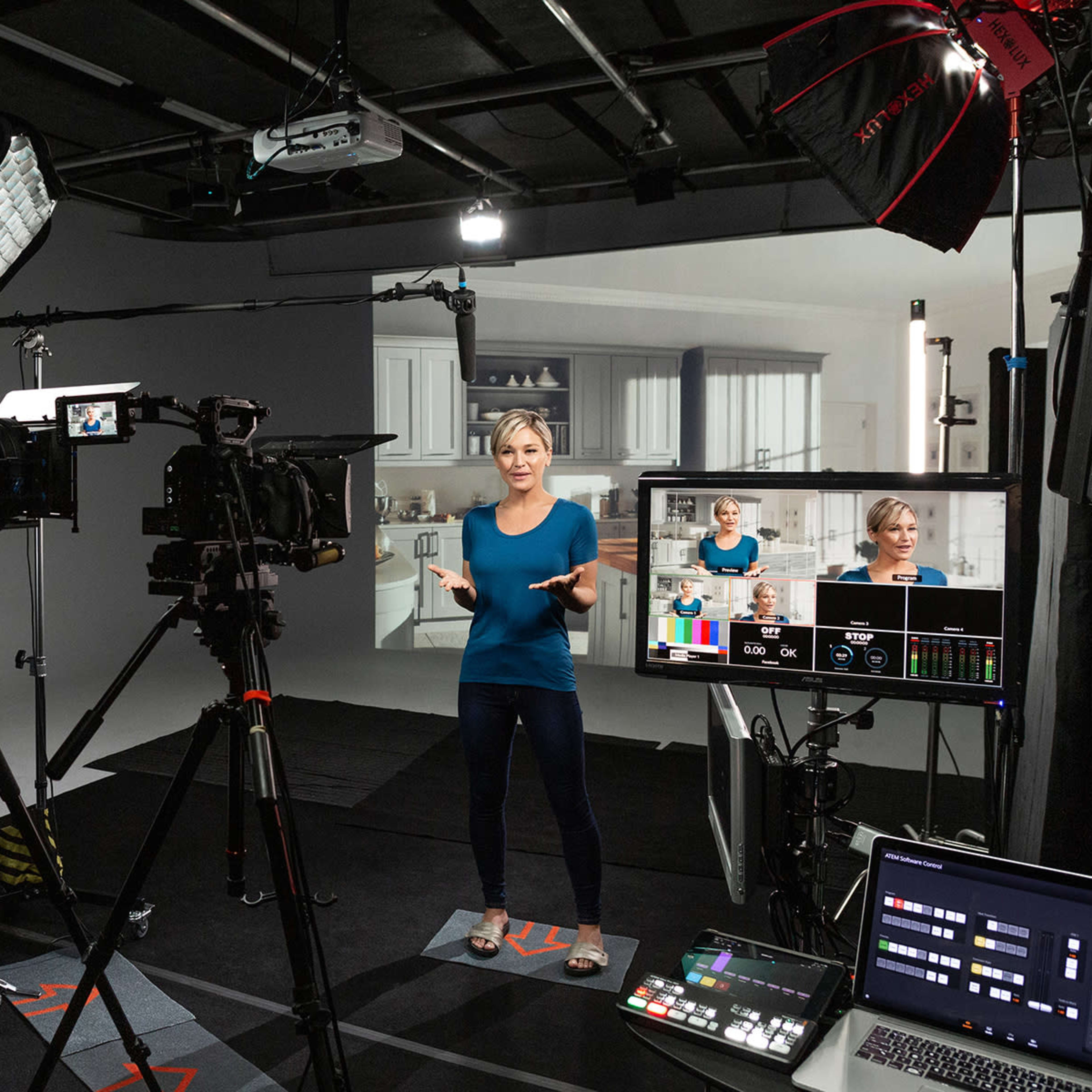 A person is filming in a studio setup with multiple cameras and lighting equipment, while a presenter stands in front of a screen displaying a kitchen background.
