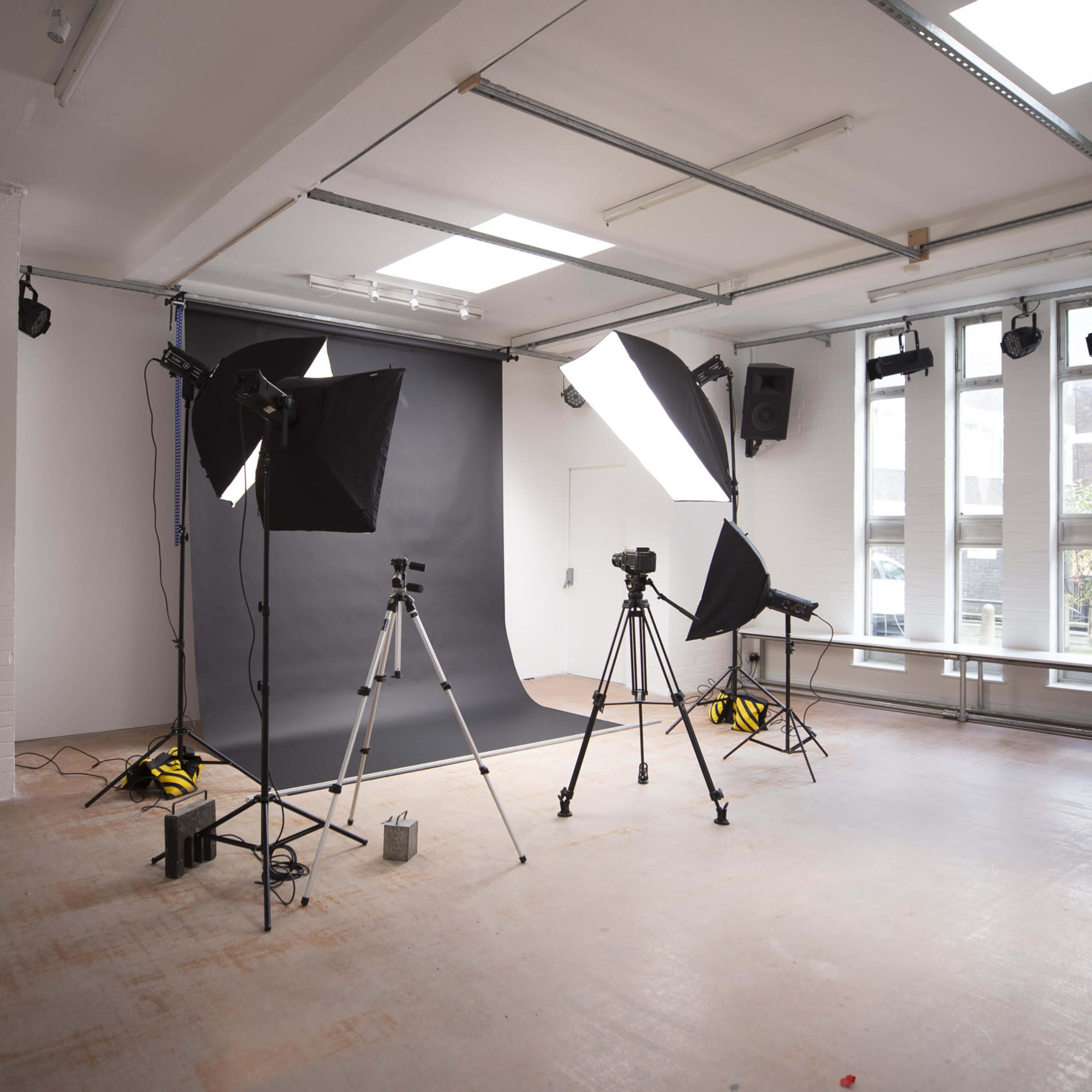 A photo studio equipped with lighting equipment, tripods, and a dark backdrop.