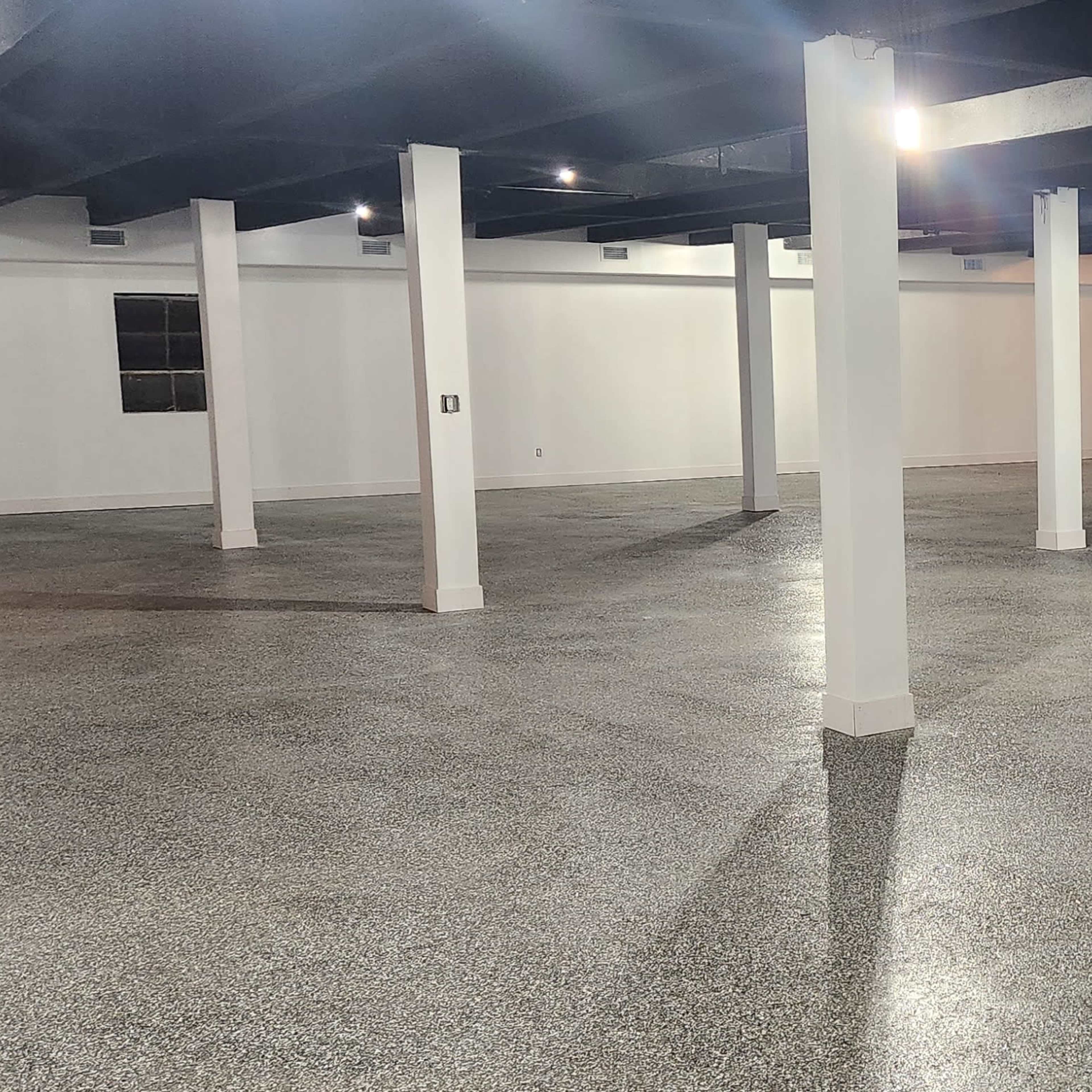 An empty, well-lit industrial space with polished concrete floors and white columns supporting a black ceiling.