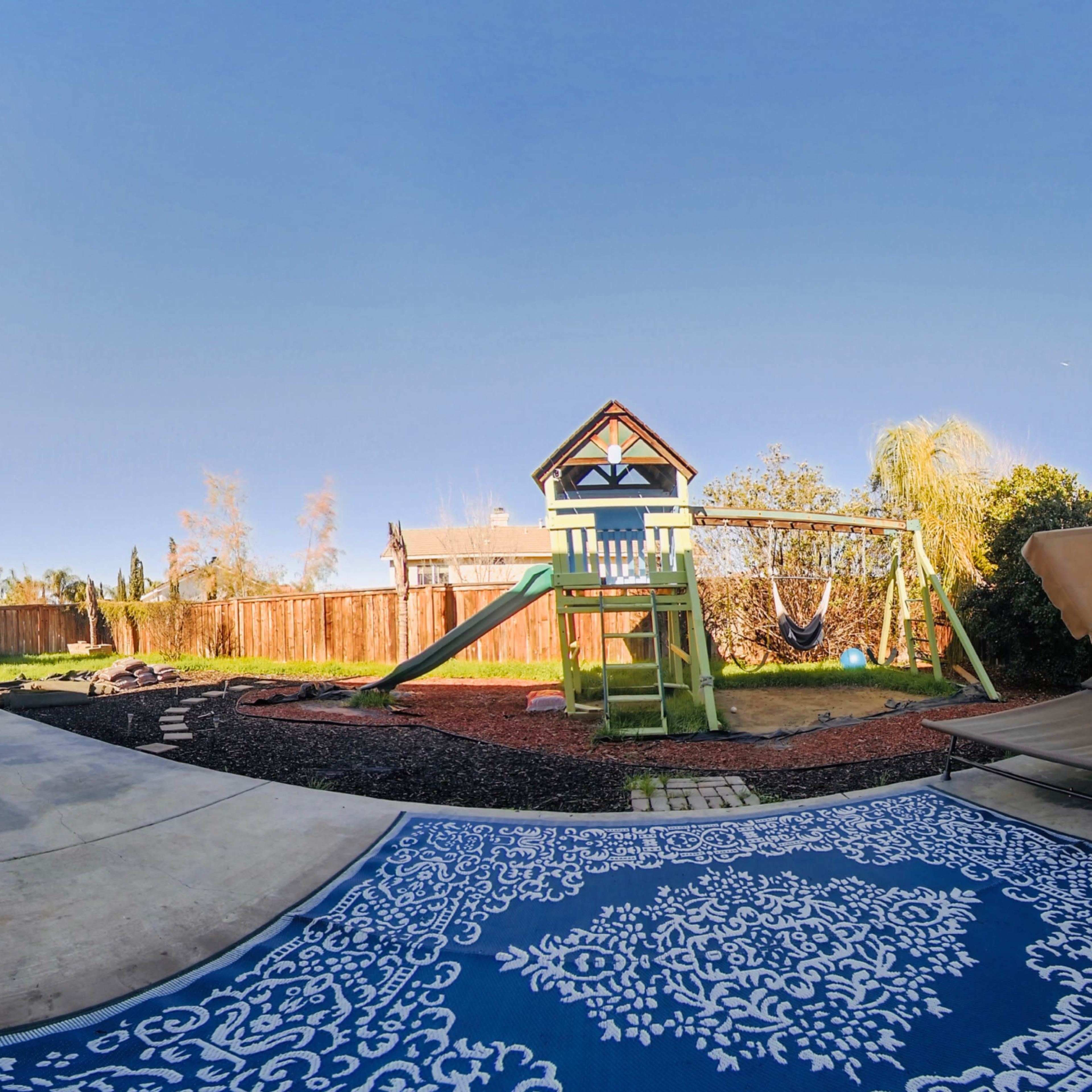 A backyard scene features a playset with a slide and swings, surrounded by landscaping and patio furniture.
