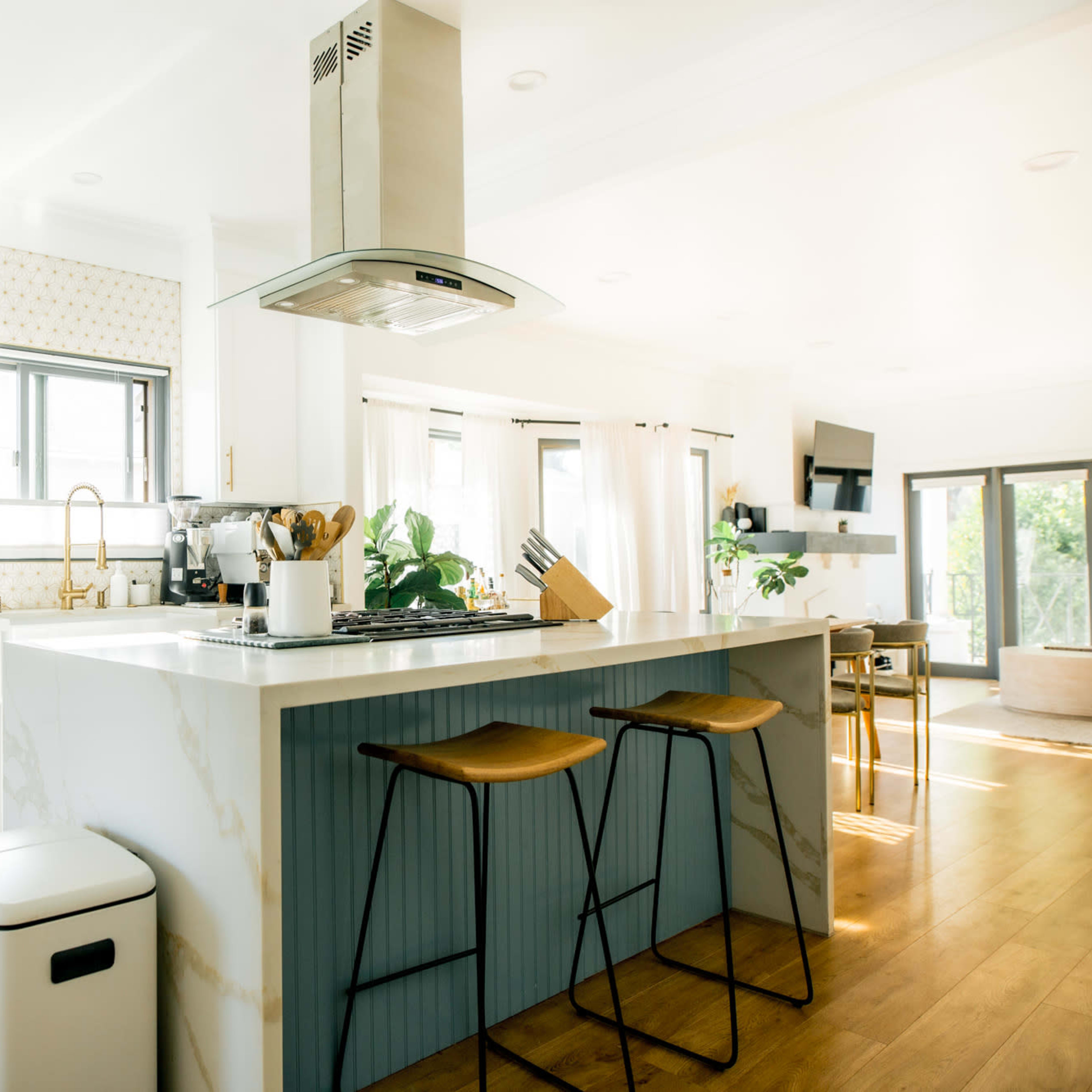 A modern kitchen features a center island with bar stools, stainless steel appliances, and light wood flooring.
