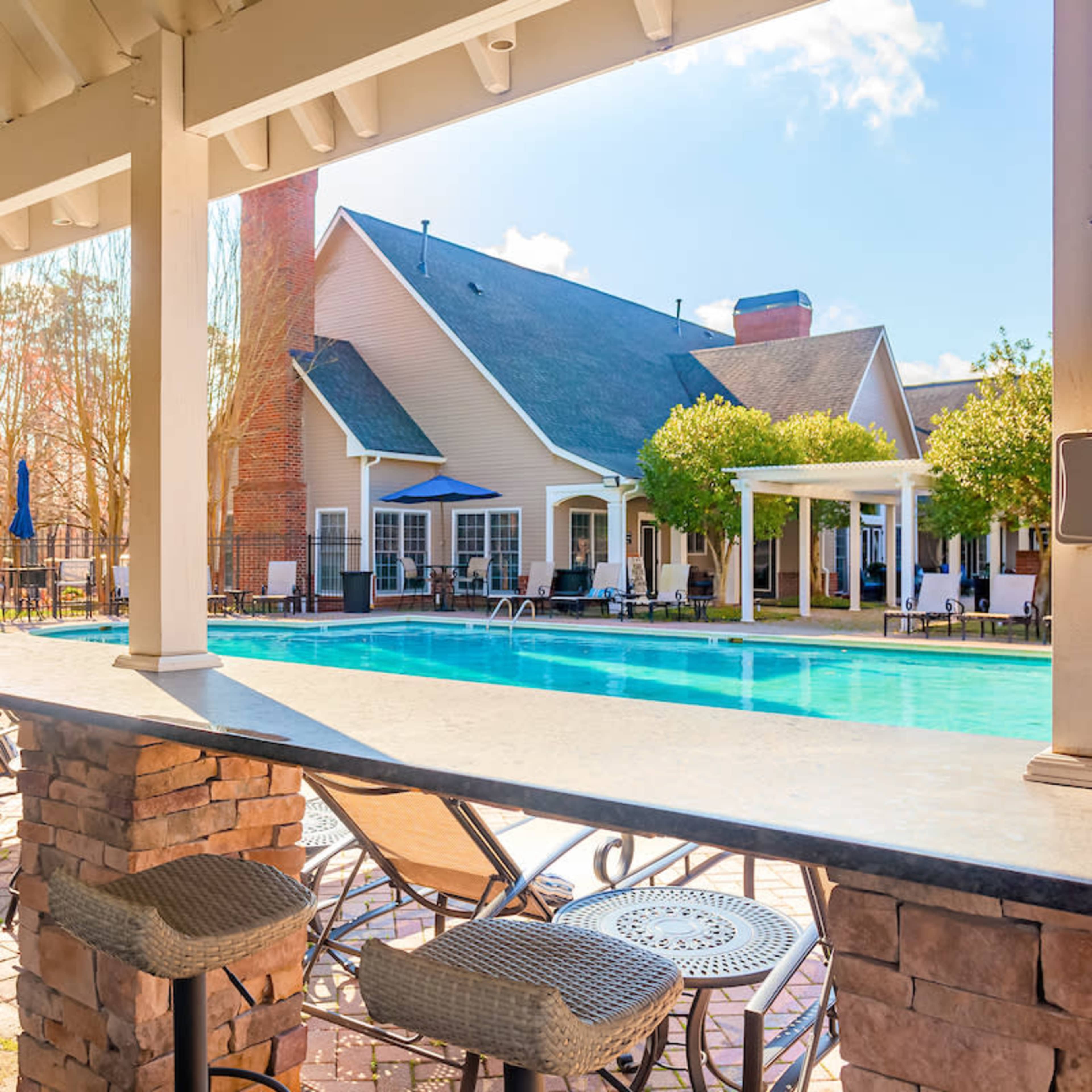 A pool area with seating and a modern clubhouse in the background under a clear blue sky.