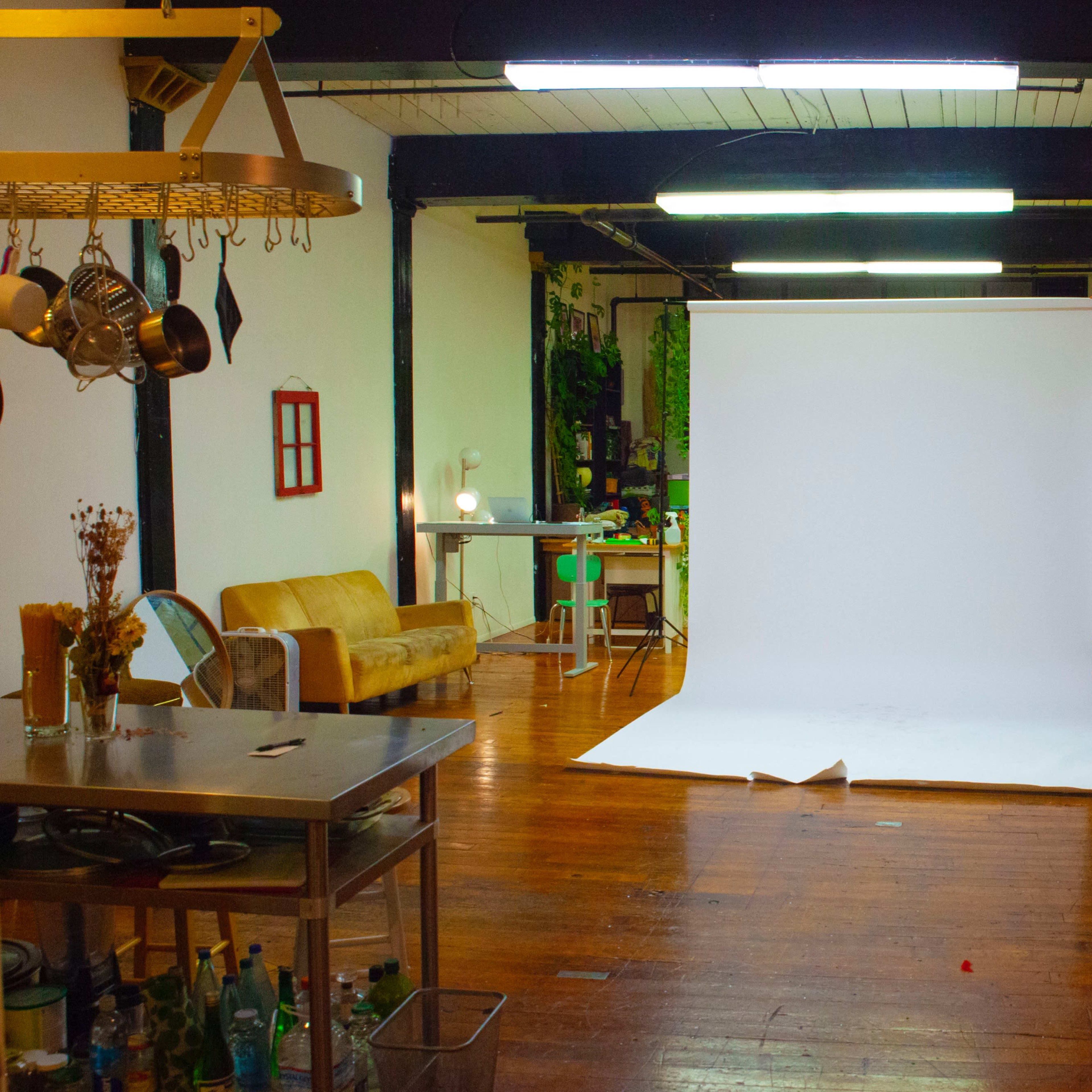 A spacious studio with a white backdrop set up in the center, surrounded by various furniture and decor elements.