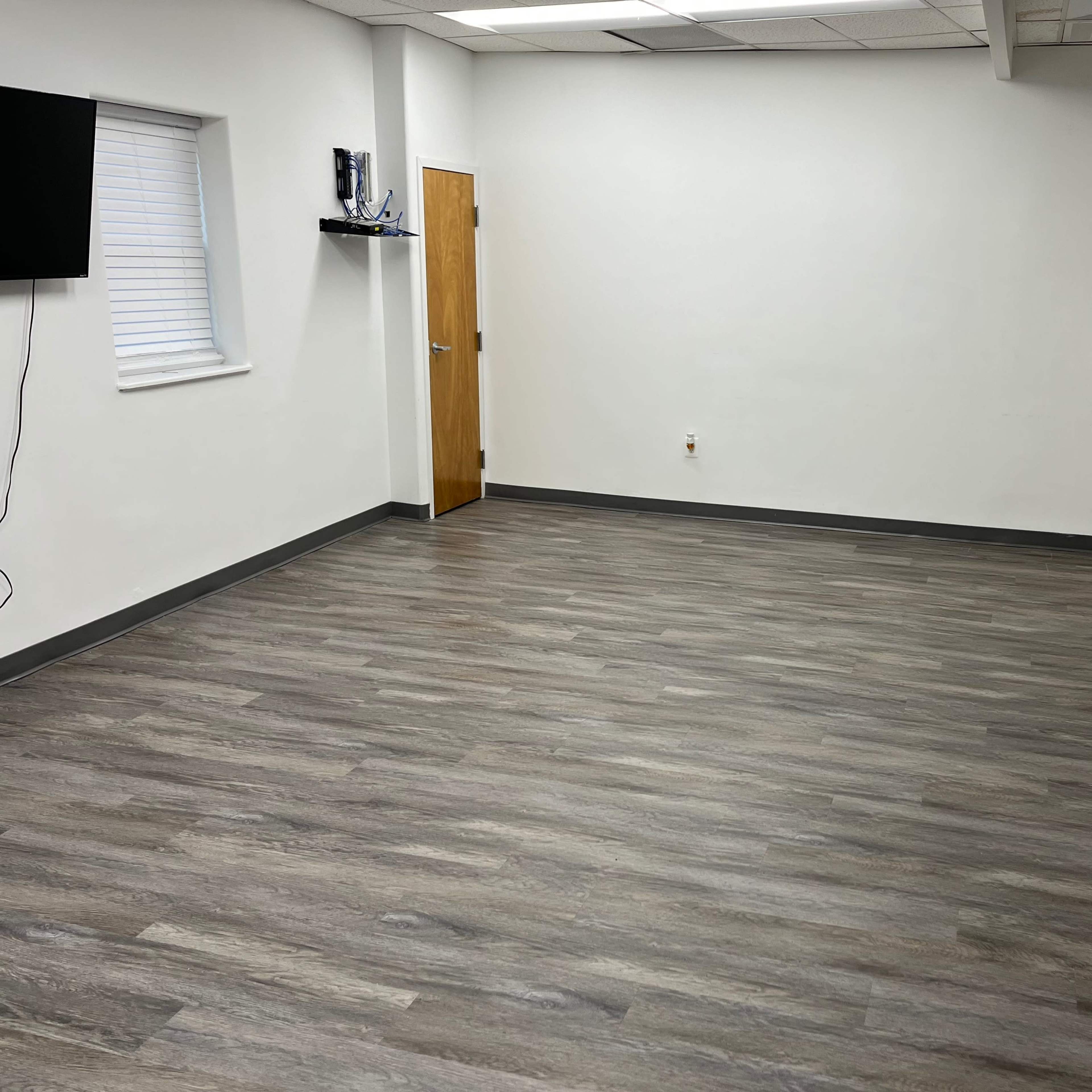 A vacant room with light gray wood flooring, white walls, and two wooden doors.