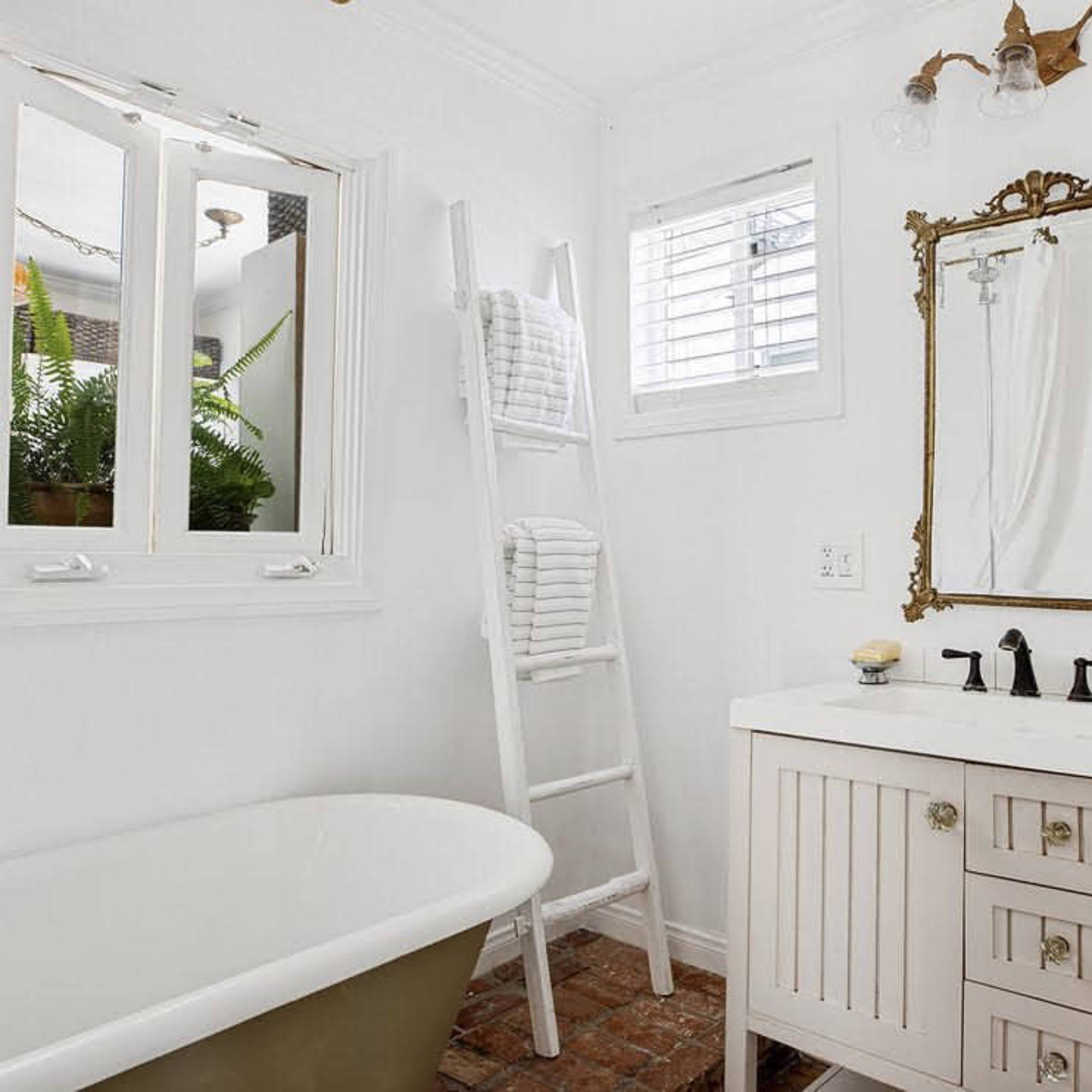 A bright bathroom featuring a freestanding bathtub, a white ladder holding neatly stacked towels, and a mirror above a vanity with sink fixtures.