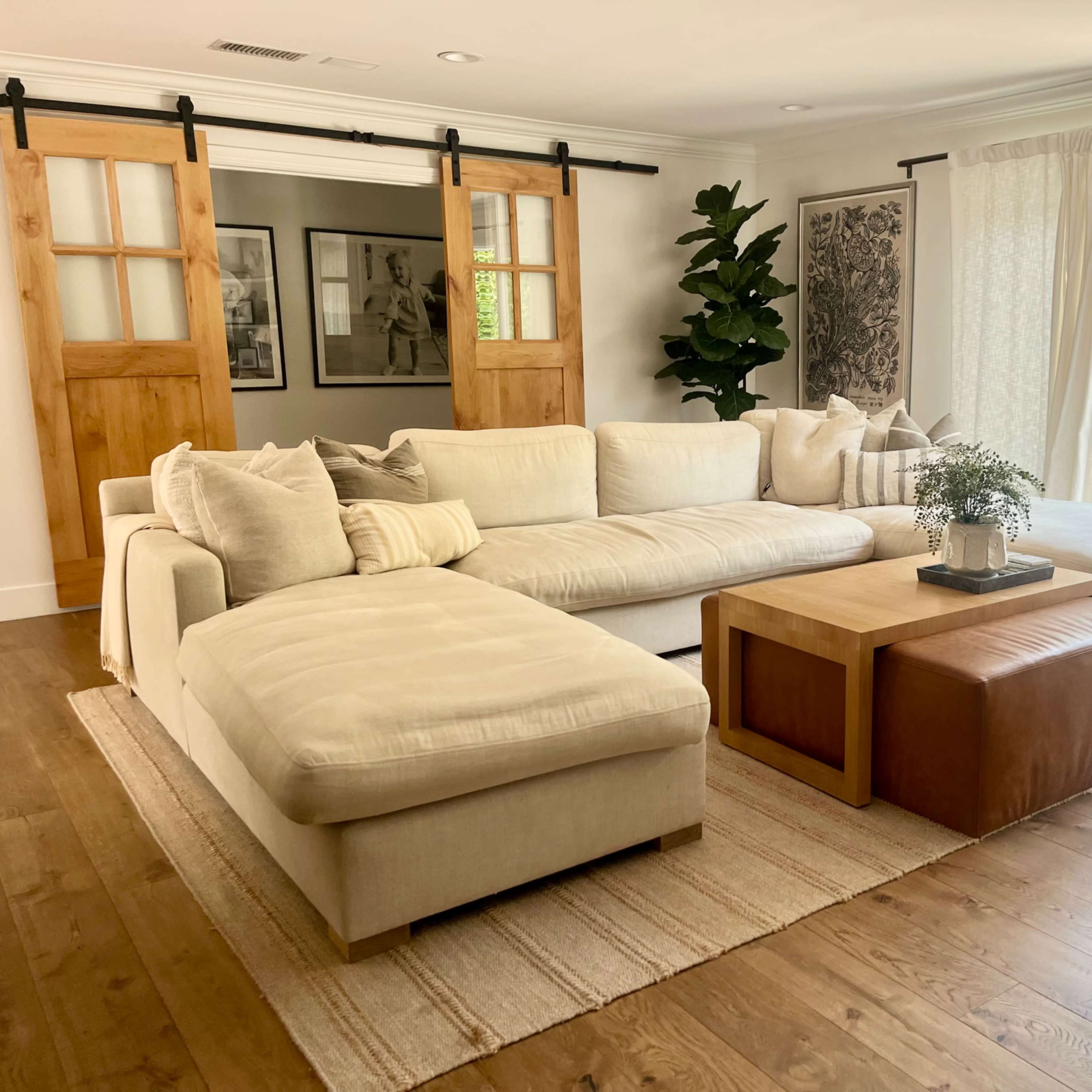 A modern living room featuring a large sectional sofa, a wooden coffee table, and sliding barn doors leading to an outdoor area.