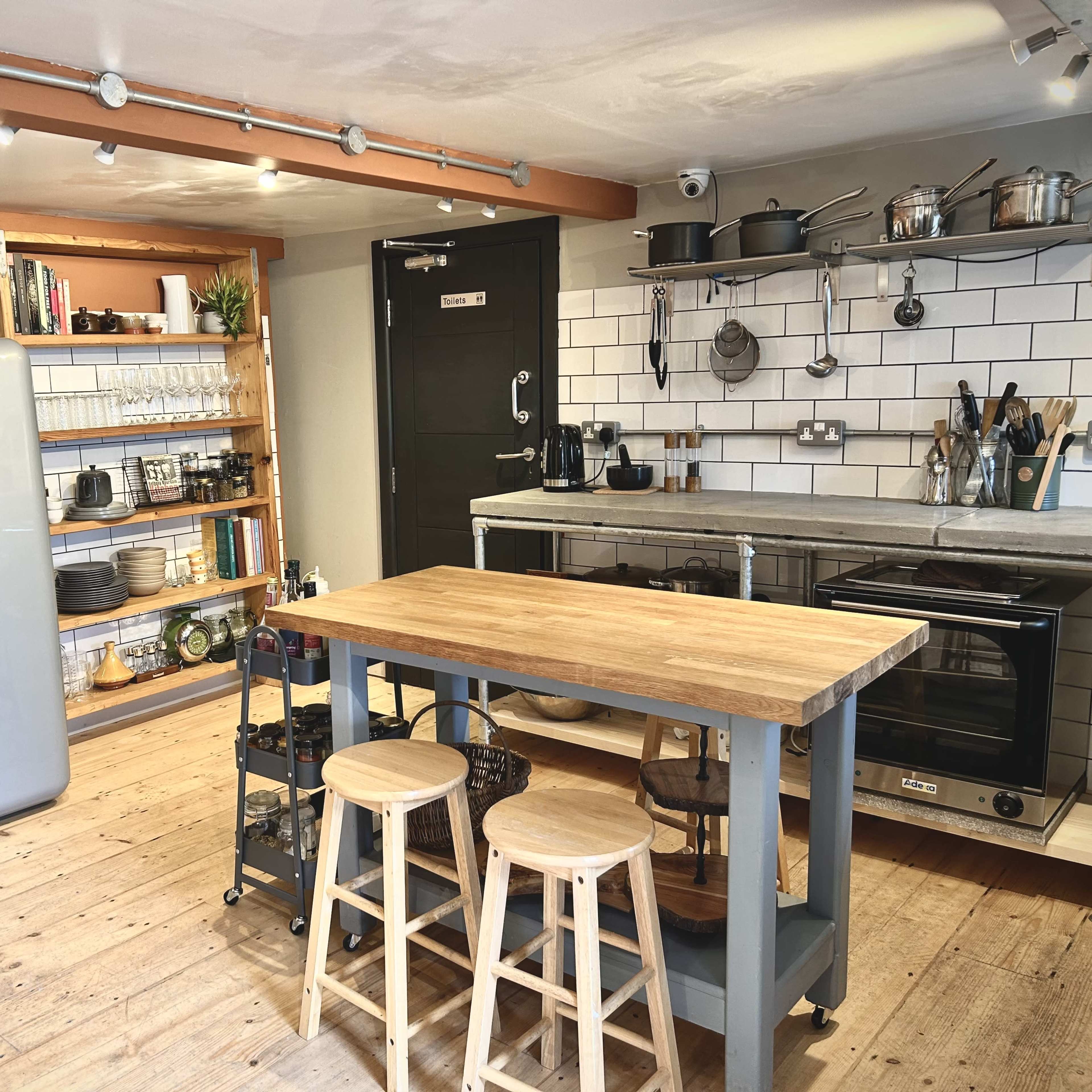 The kitchen features a retro-style refrigerator, a wooden dining table with stools, and open shelving displaying various kitchen items.