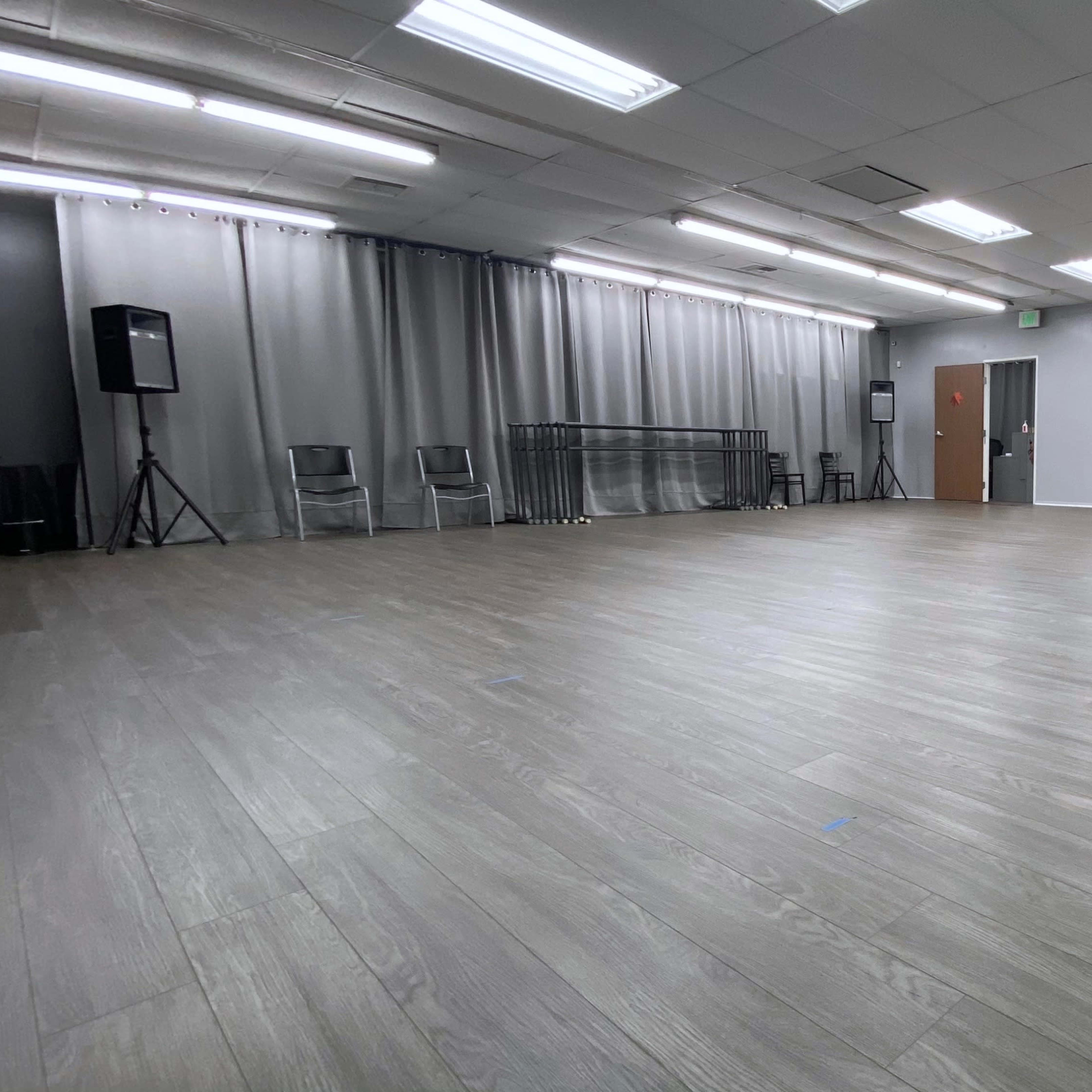 An empty dance studio with wooden flooring, gray walls, and a large mirror on one side.