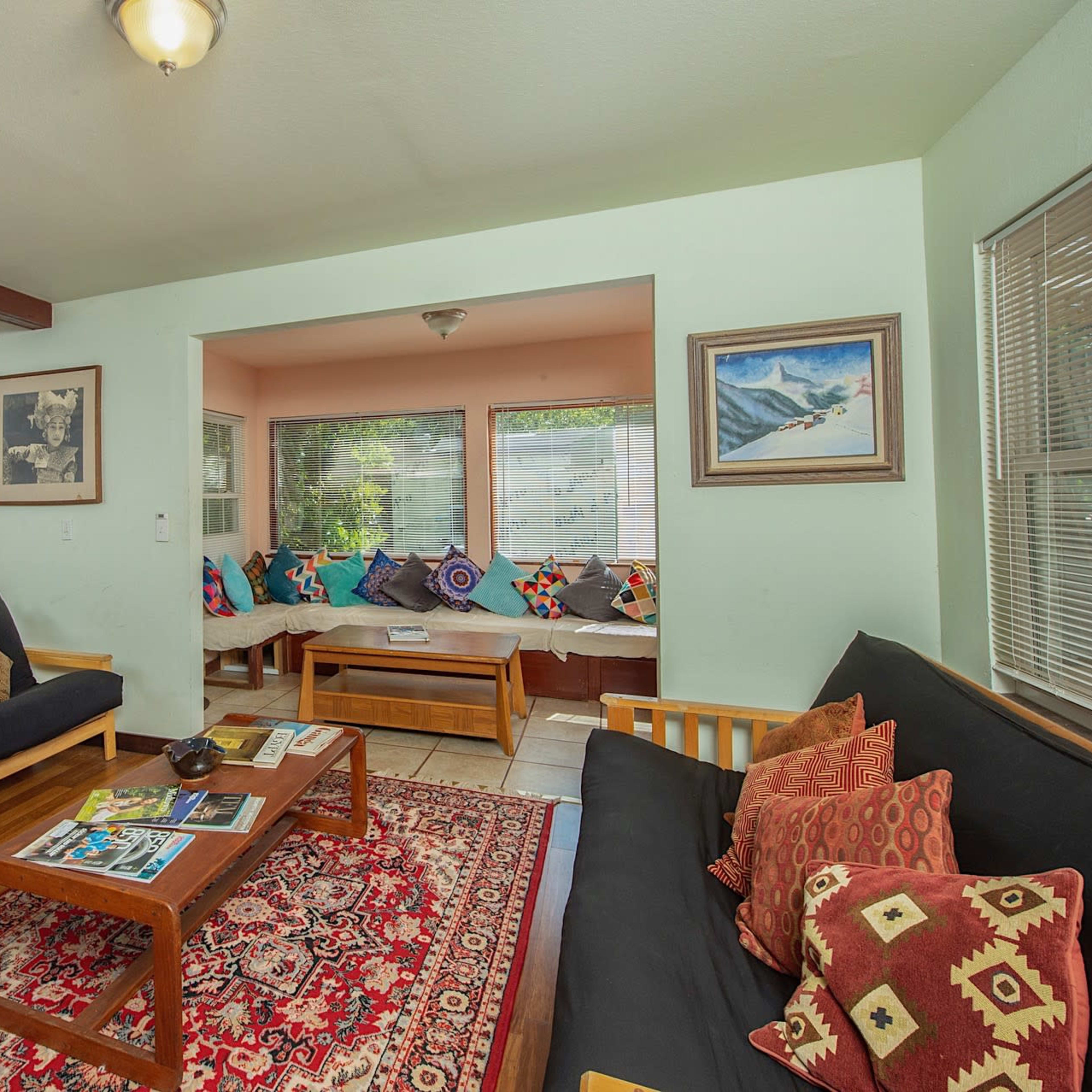 The living room features two wooden sofas with patterned cushions, a coffee table, and a window nook with colorful pillows.