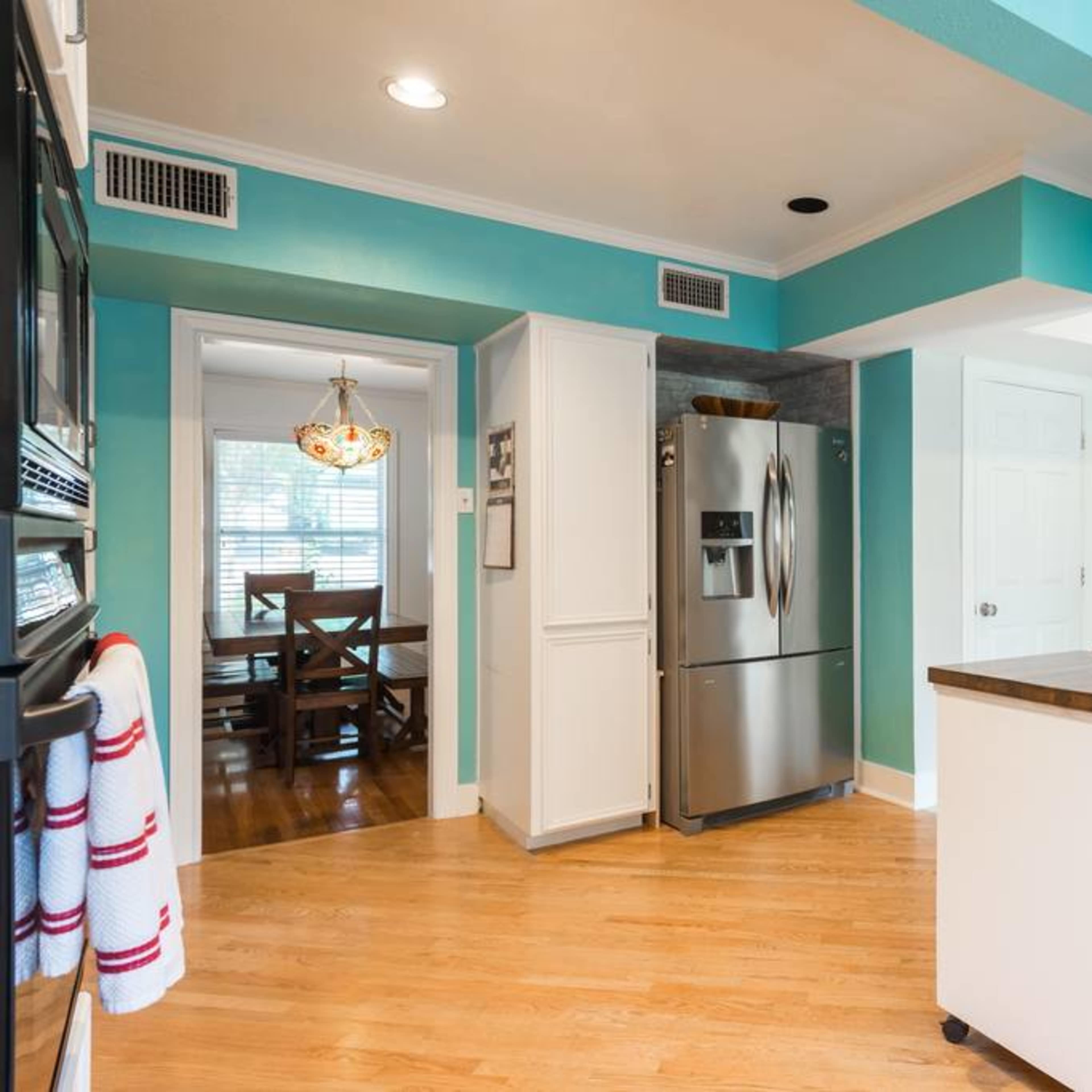 A bright kitchen with teal walls, stainless steel appliances, a wooden countertop, and a view into a dining area.