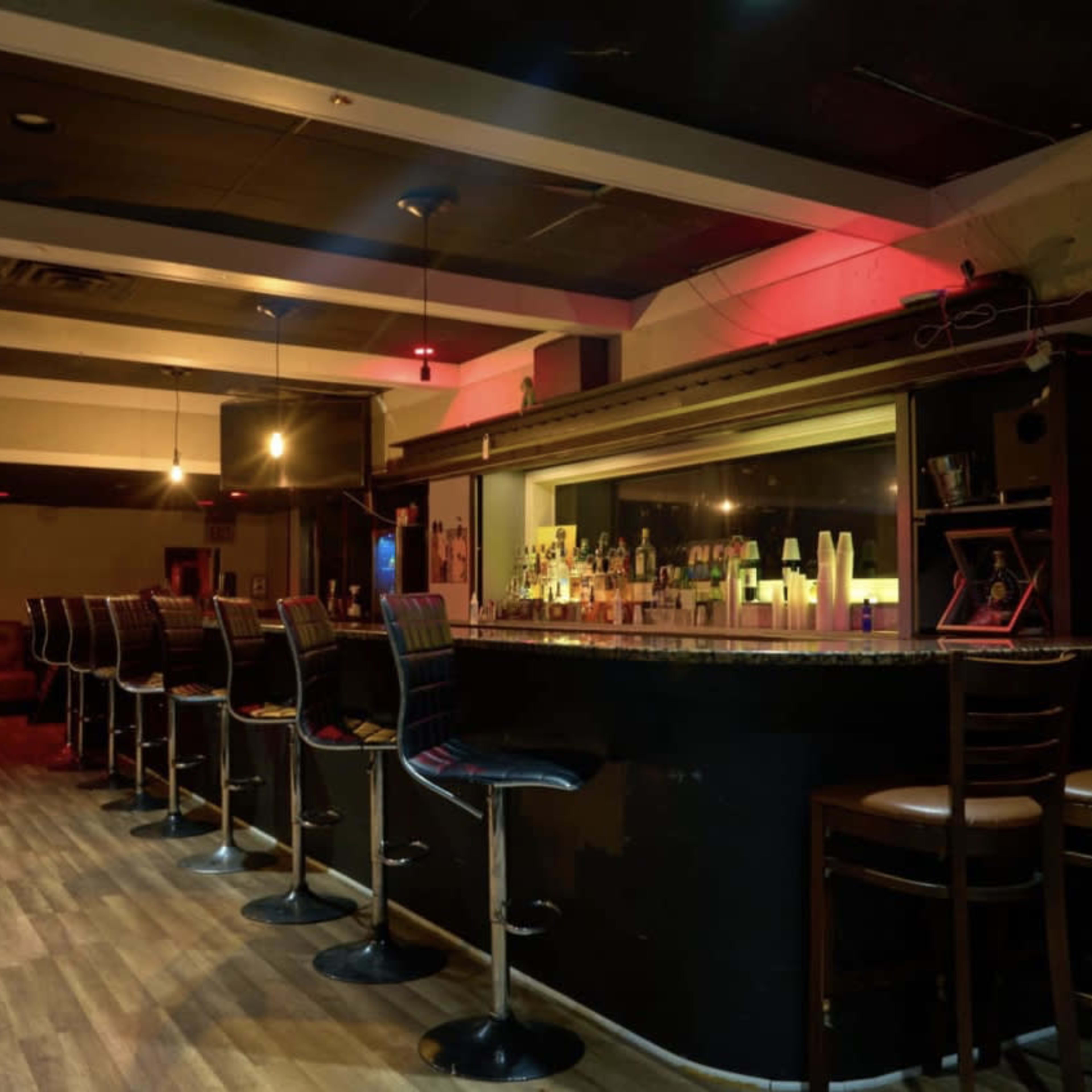 An empty bar with several high-backed chairs arranged along a dark countertop, illuminated by soft lighting.