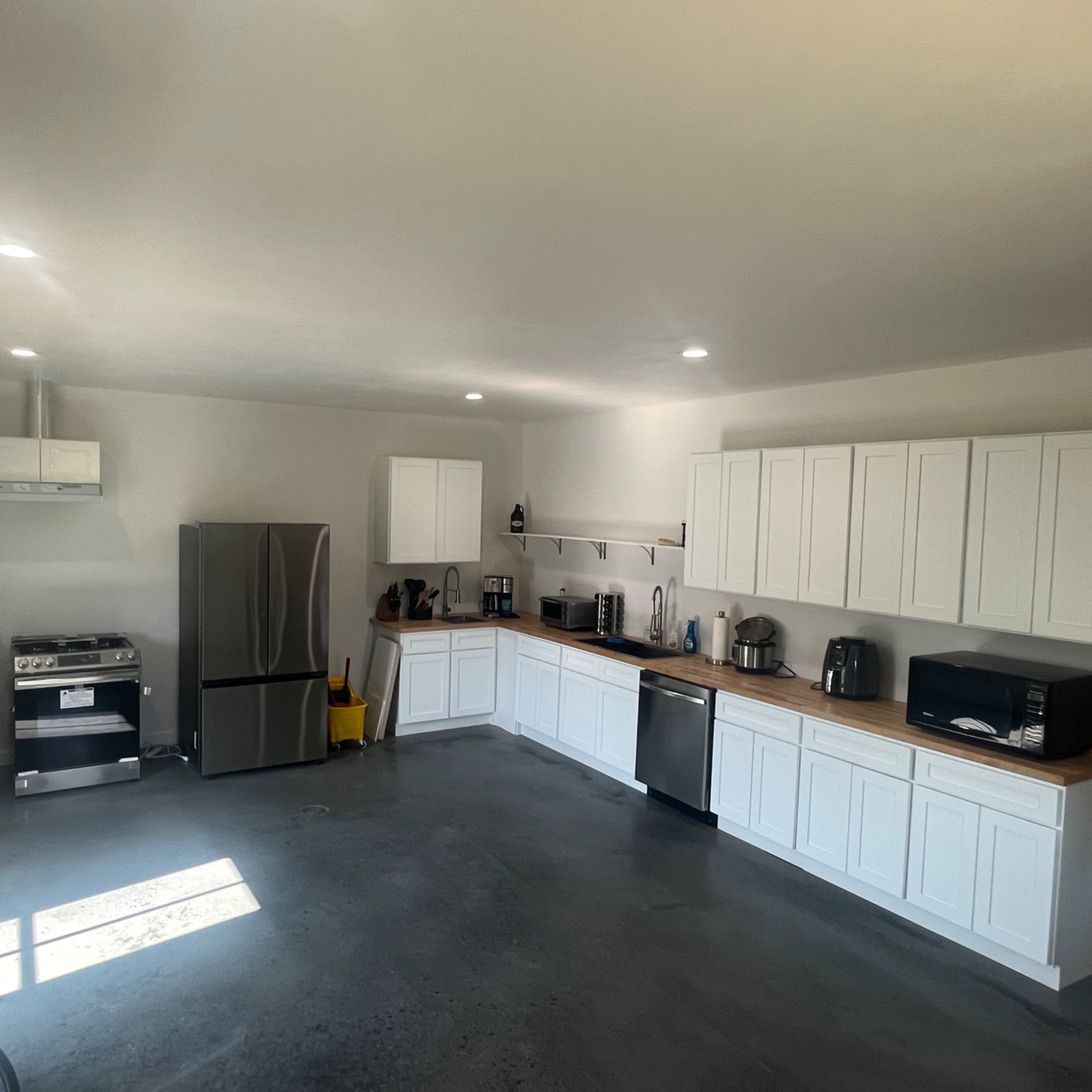 A modern kitchen features white cabinets, stainless steel appliances, and a concrete floor.