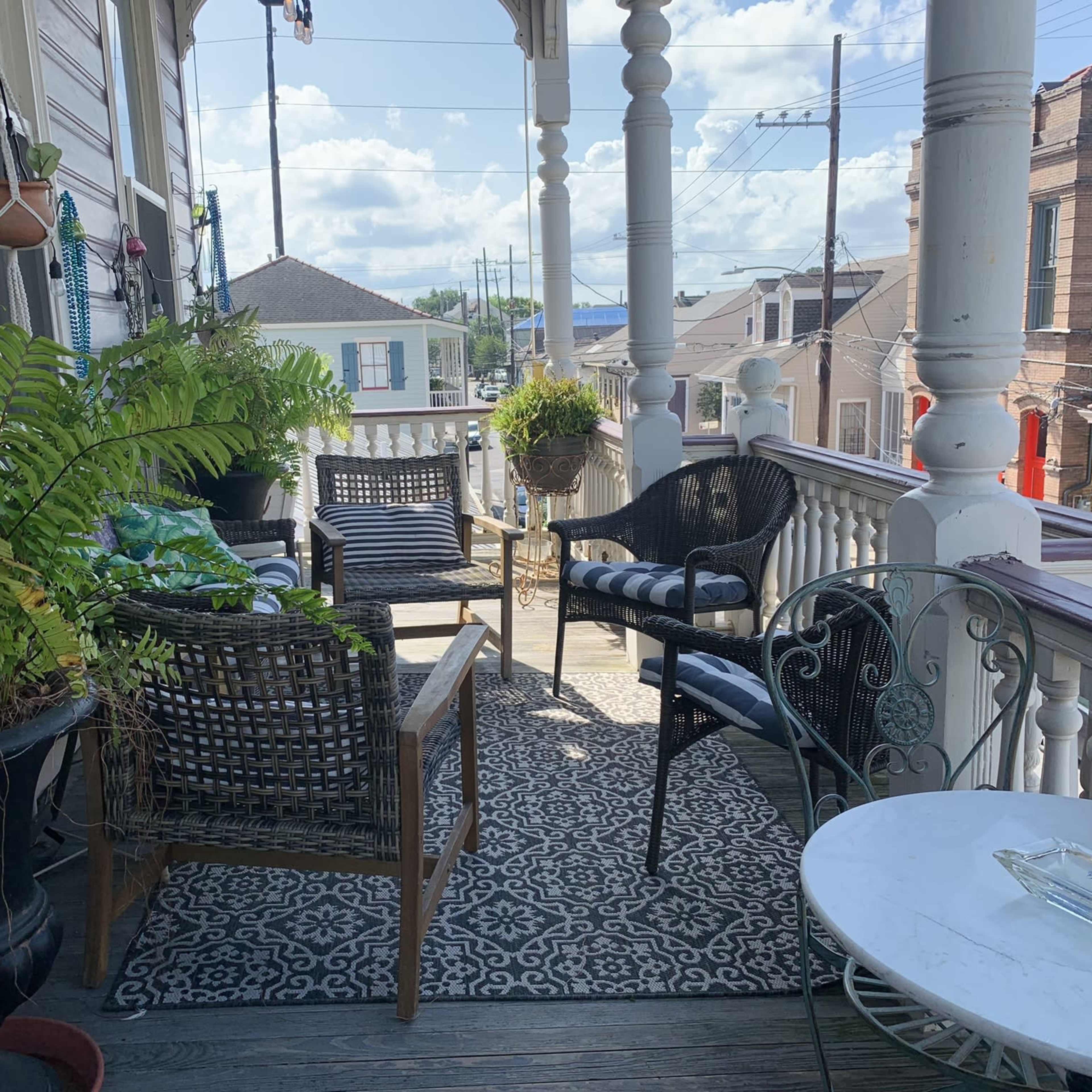 A porch features wicker chairs and a small table surrounded by potted plants and a decorative rug.