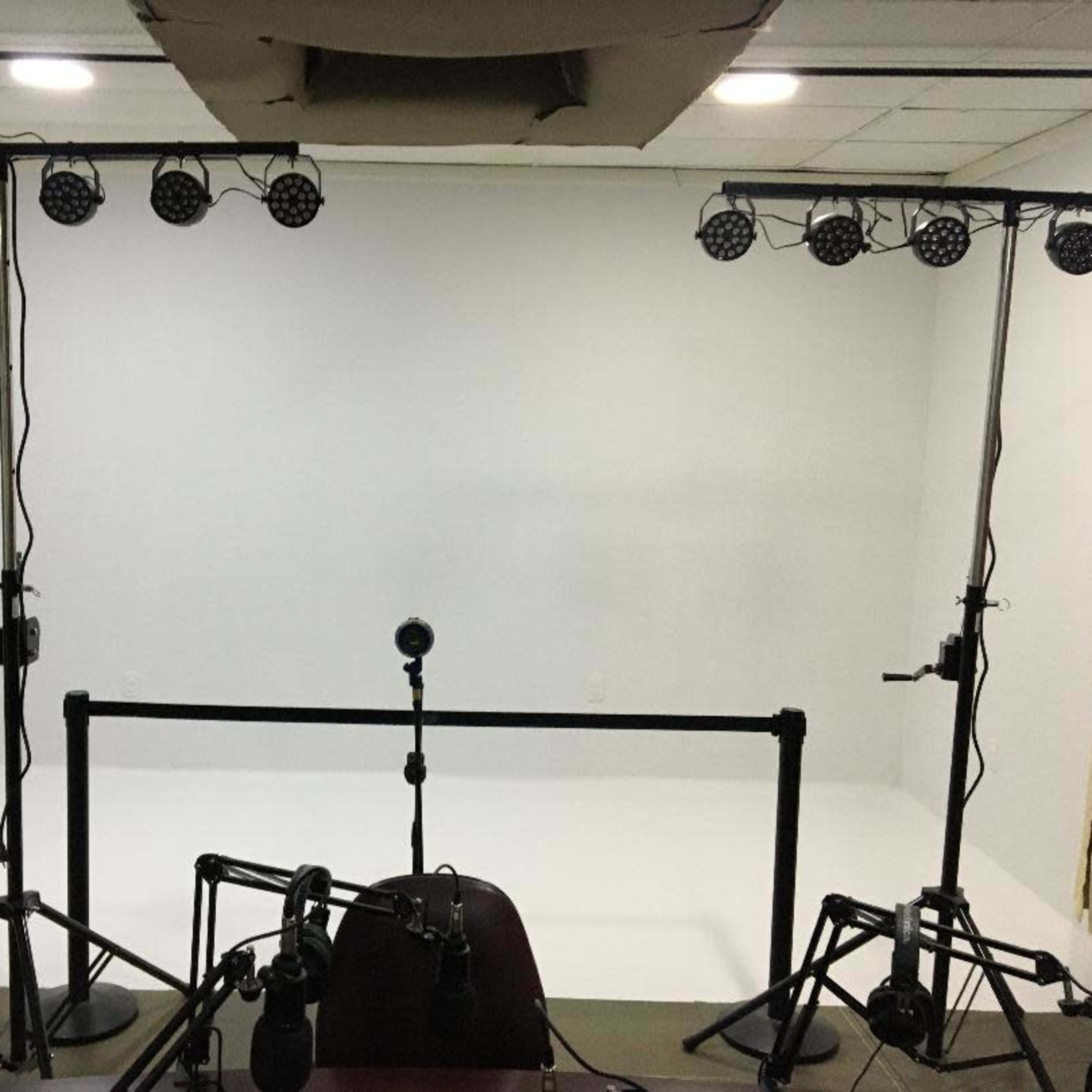 A bare studio space with a white backdrop, lighting stands equipped with multiple lights, and a microphone setup on a table.