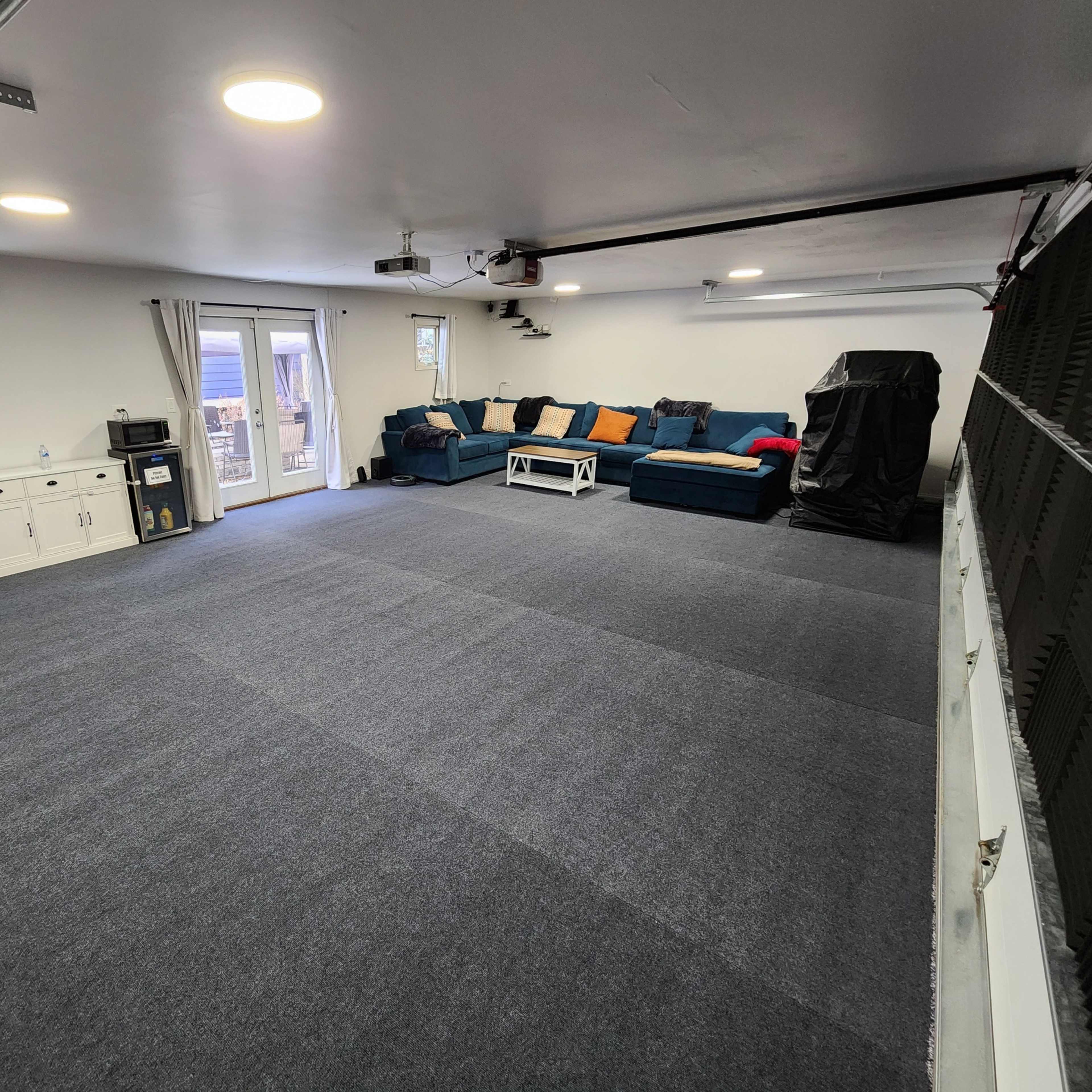A spacious room with gray carpeting, a blue sofa set against the wall, and sliding glass doors leading to an outdoor area.