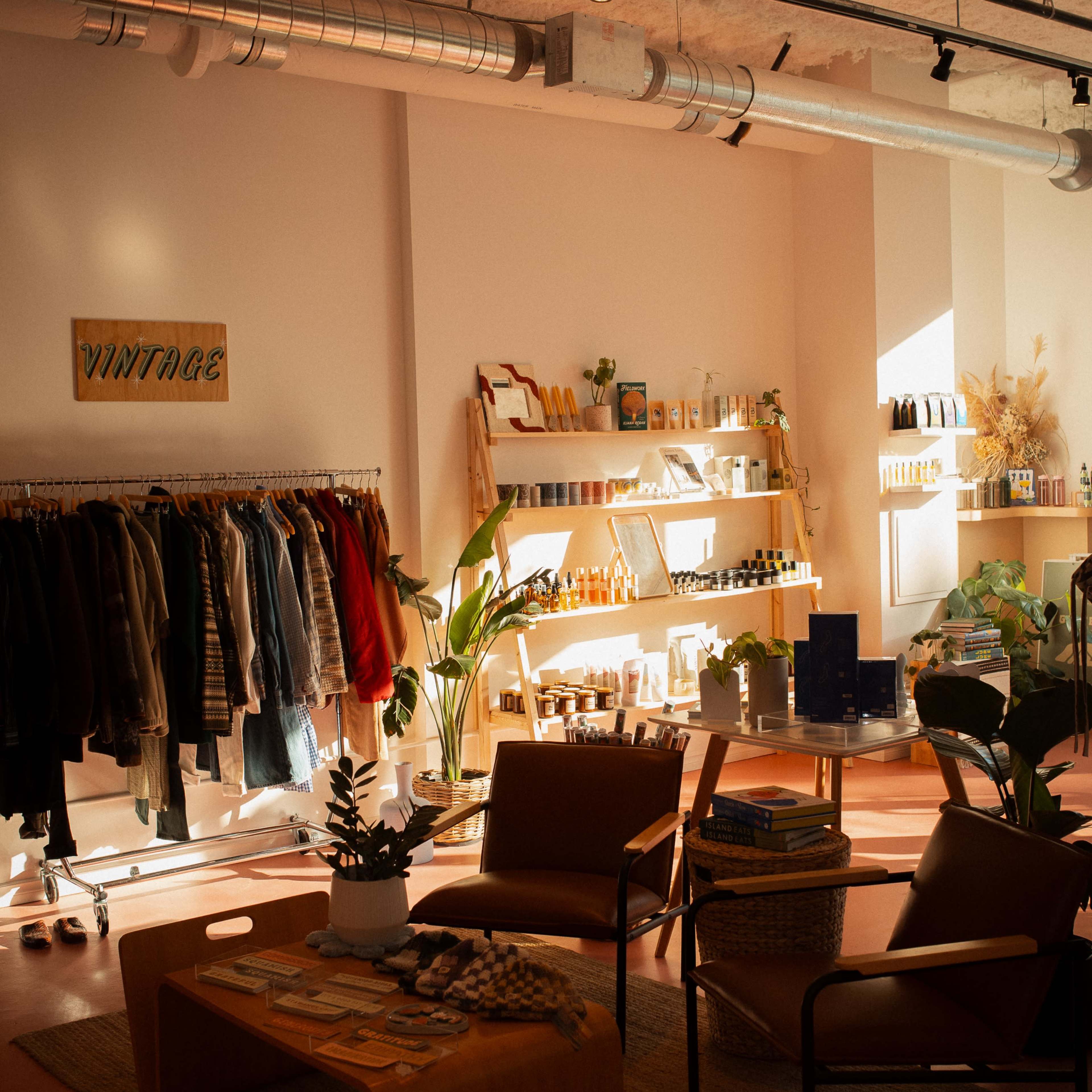 A vintage-style shop interior featuring clothing racks, shelves lined with products, and seating areas with plants and decor.