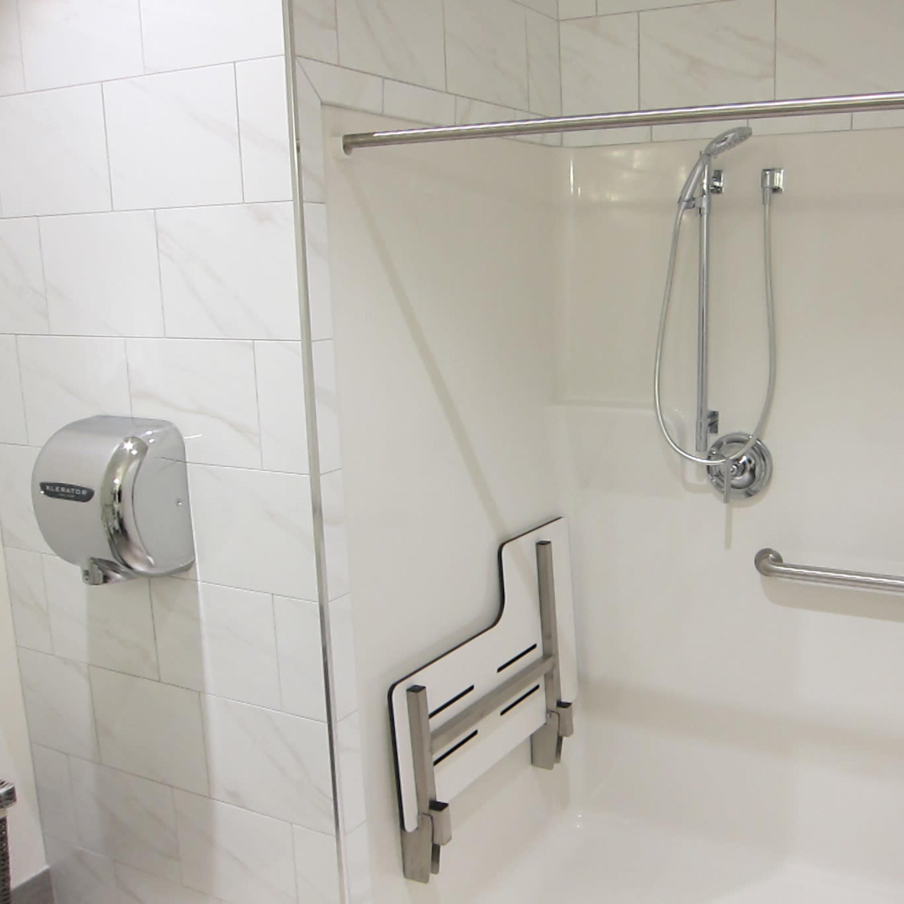 A shower stall equipped with a foldable shower seat, grab bars, a handheld showerhead, and a shower curtain.