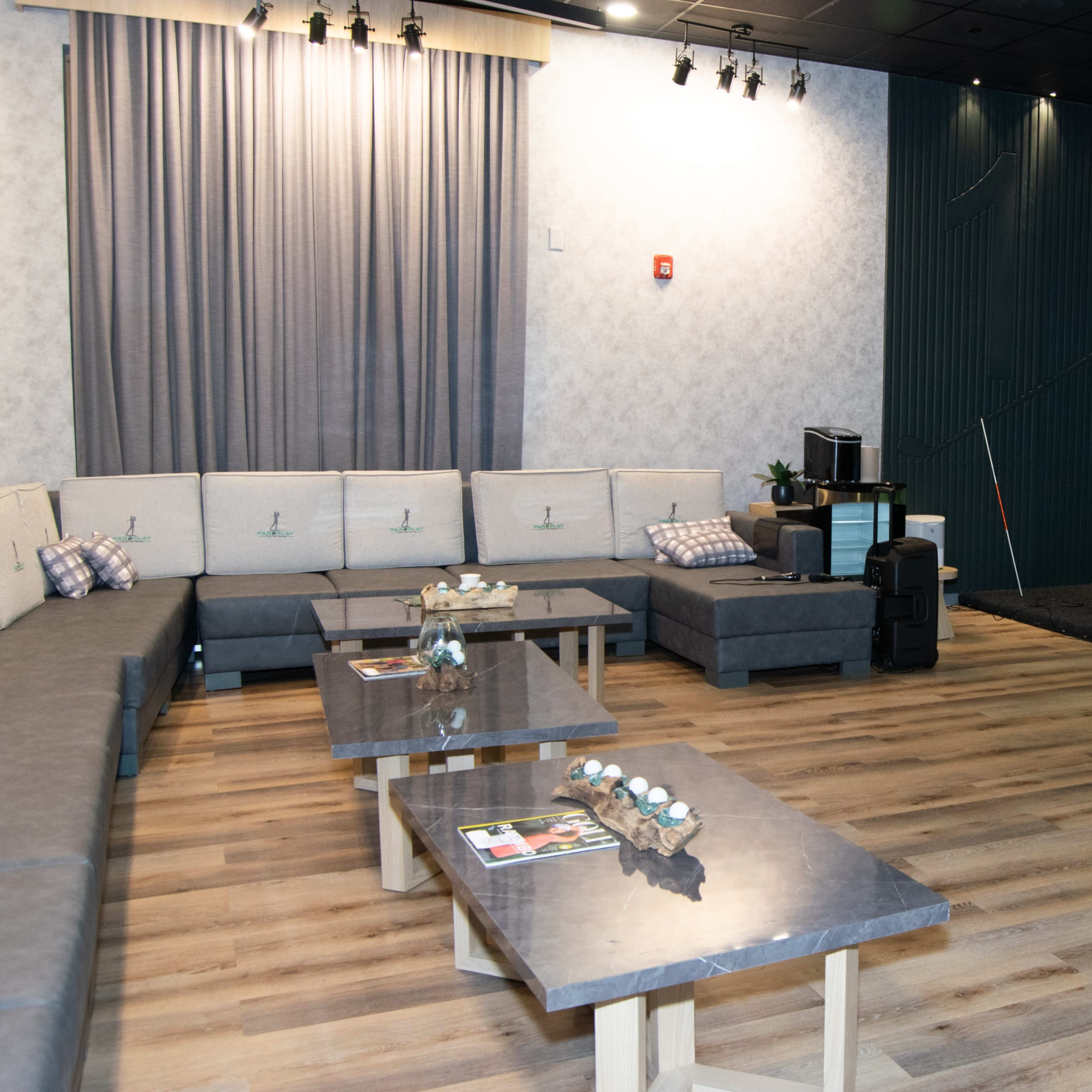 A modern lounge area with a sectional sofa, low tables, and a space with a putting green in the corner.