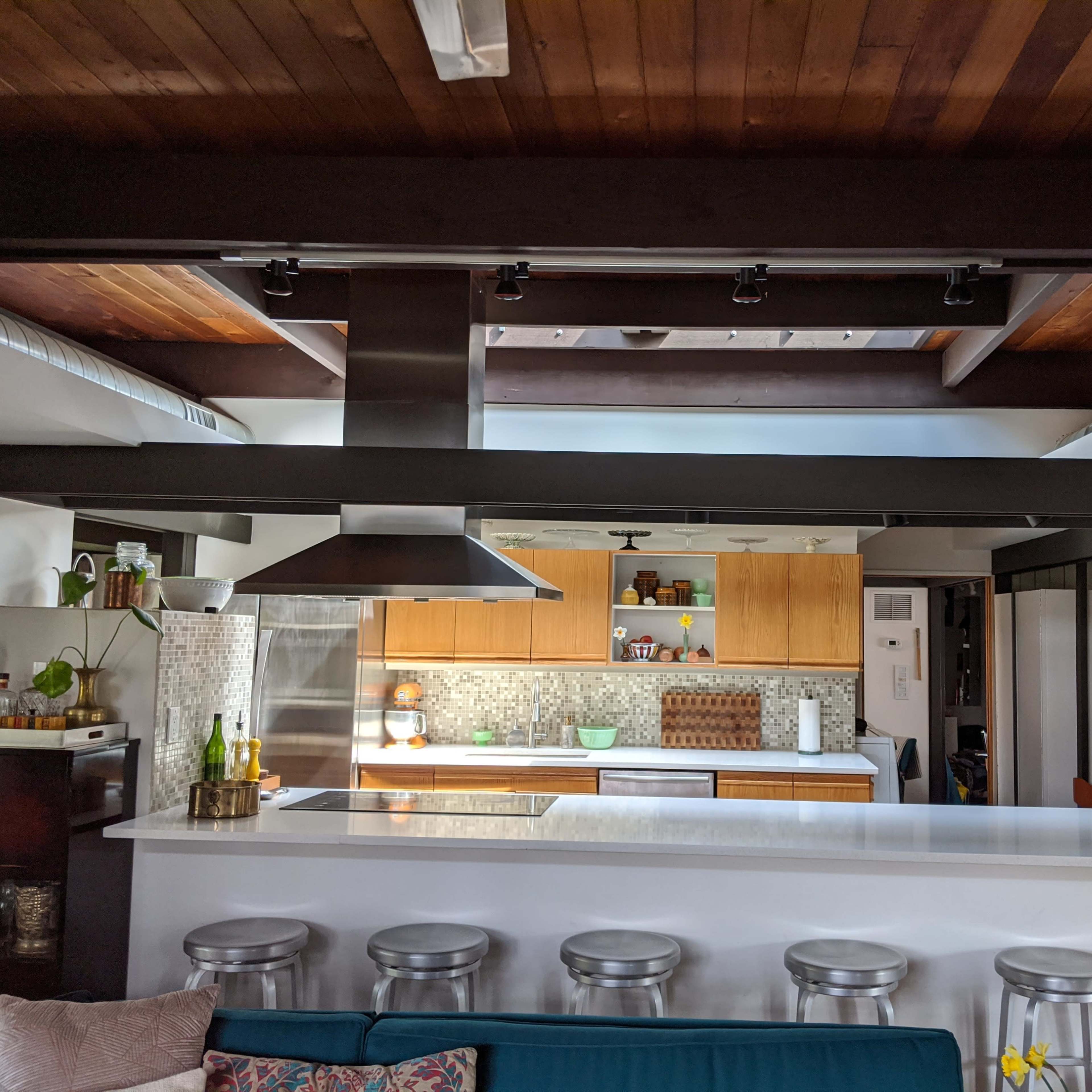 A modern kitchen with wooden cabinets, a white countertop, and metal bar stools arranged around a kitchen island.