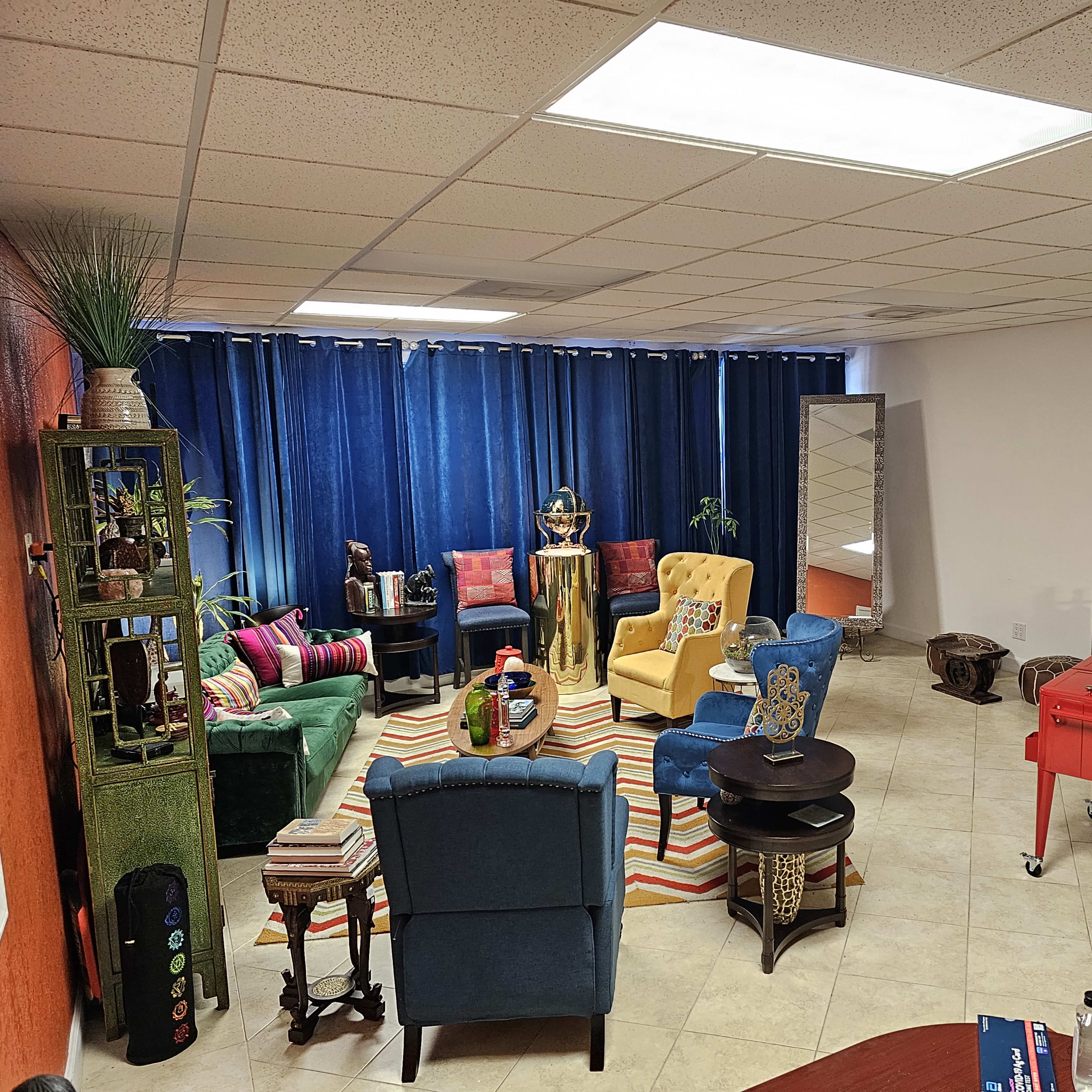 A vibrant room features colorful furniture, including a yellow and blue chair, a striped rug, and a bar cart, with large blue curtains covering a window.
