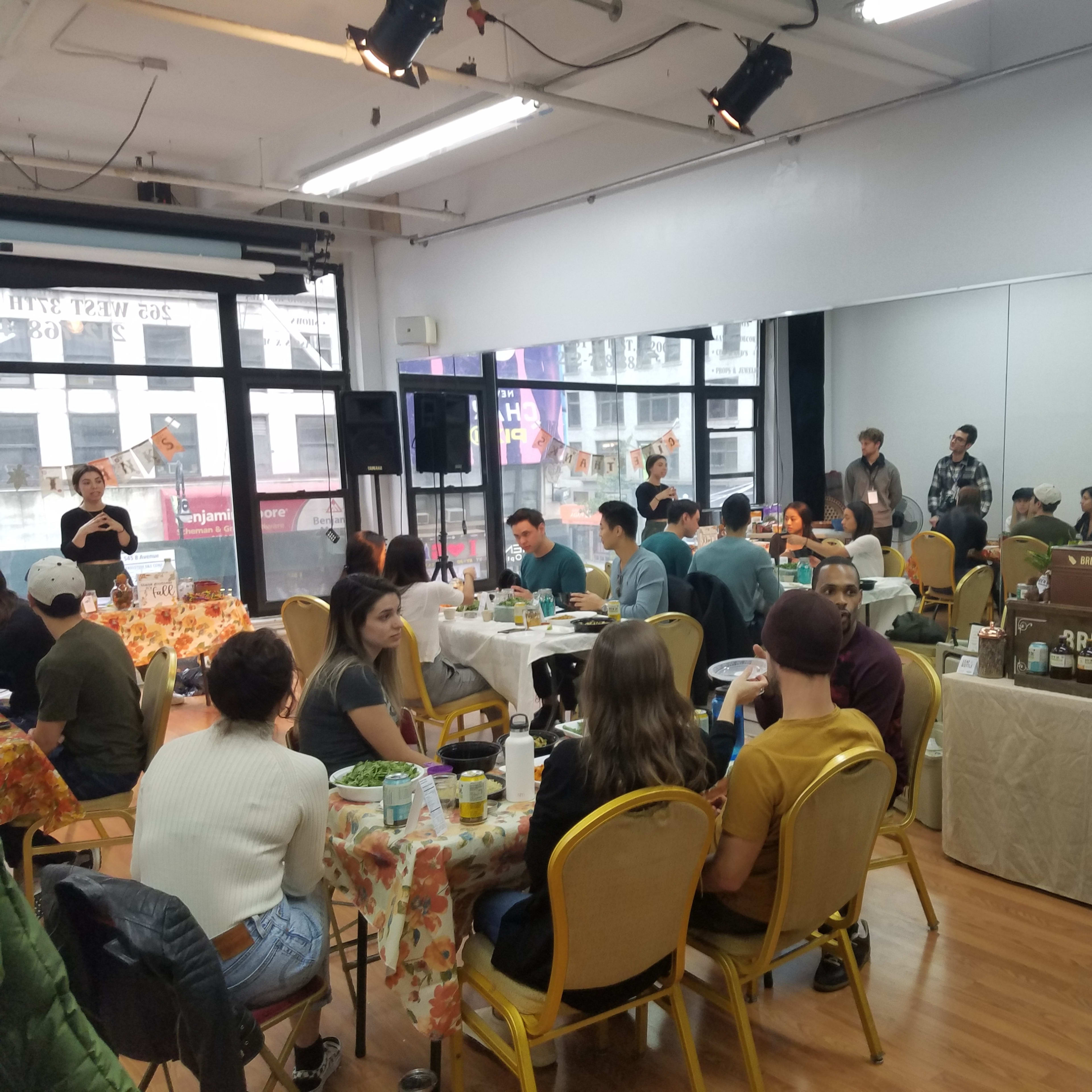 A group of people sit at tables in a bright, open room decorated with autumn-themed decor.