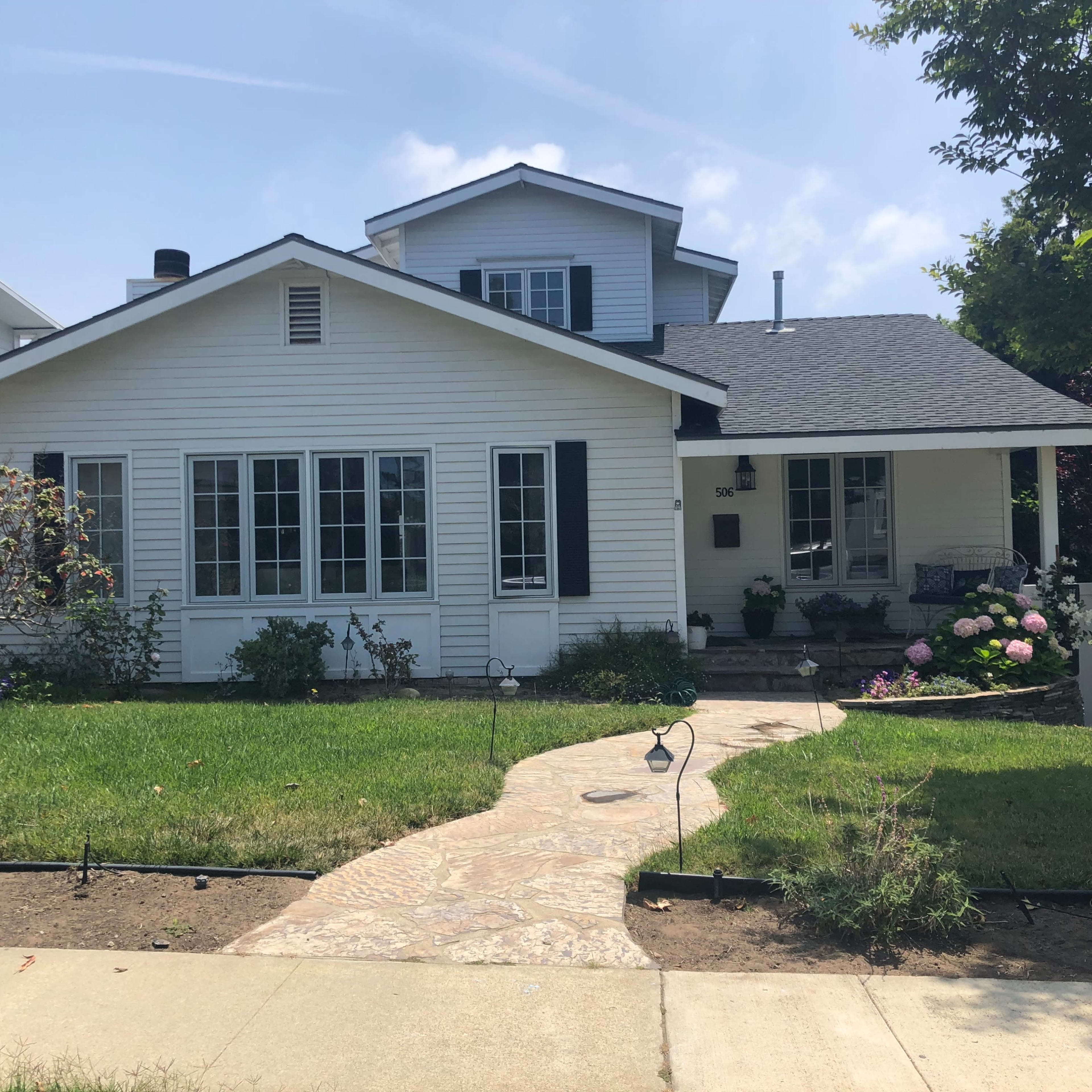 A white wooden house with multiple windows and a neatly landscaped front yard featuring a stone pathway.