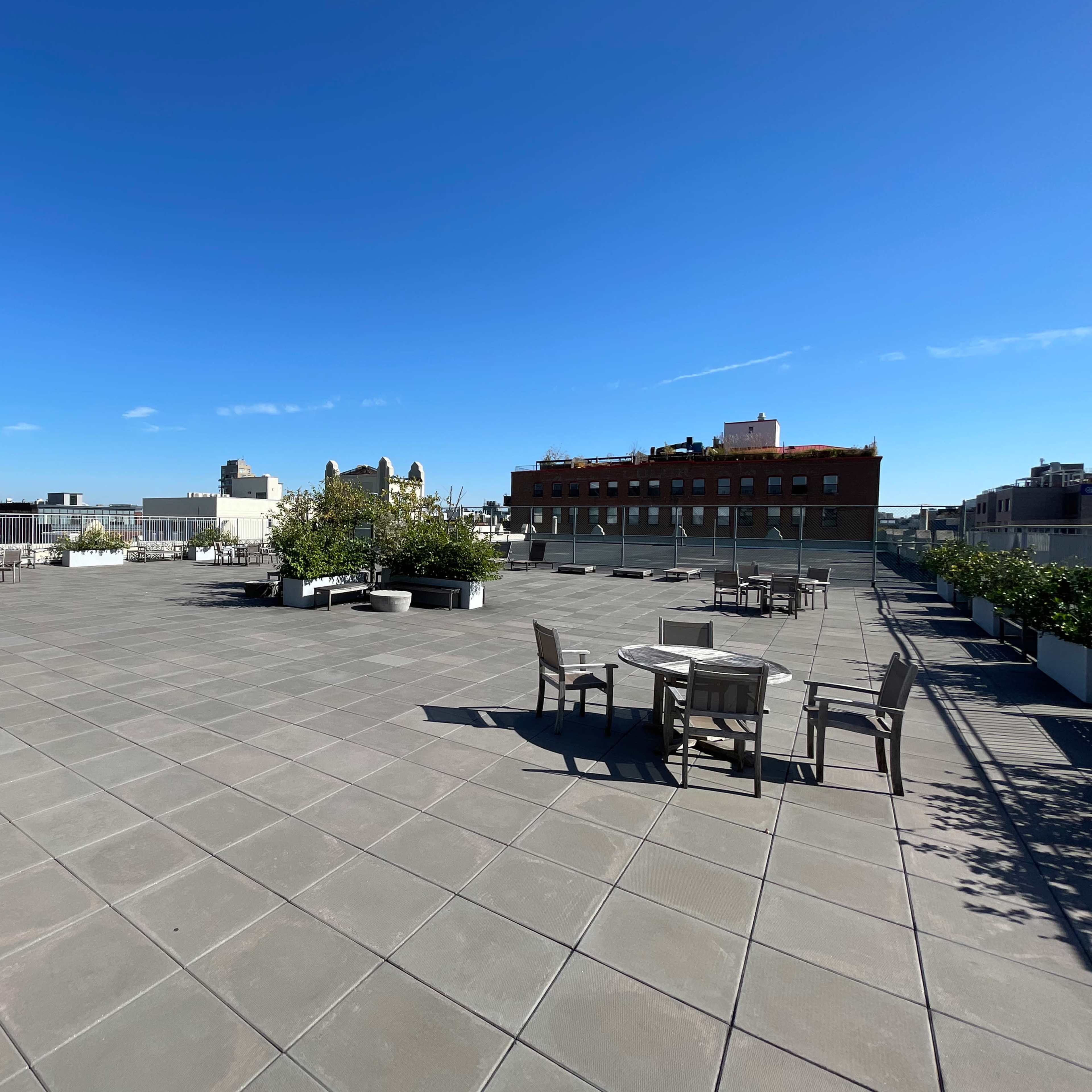 A spacious rooftop terrace features outdoor seating, planters, and a clear blue sky overhead.