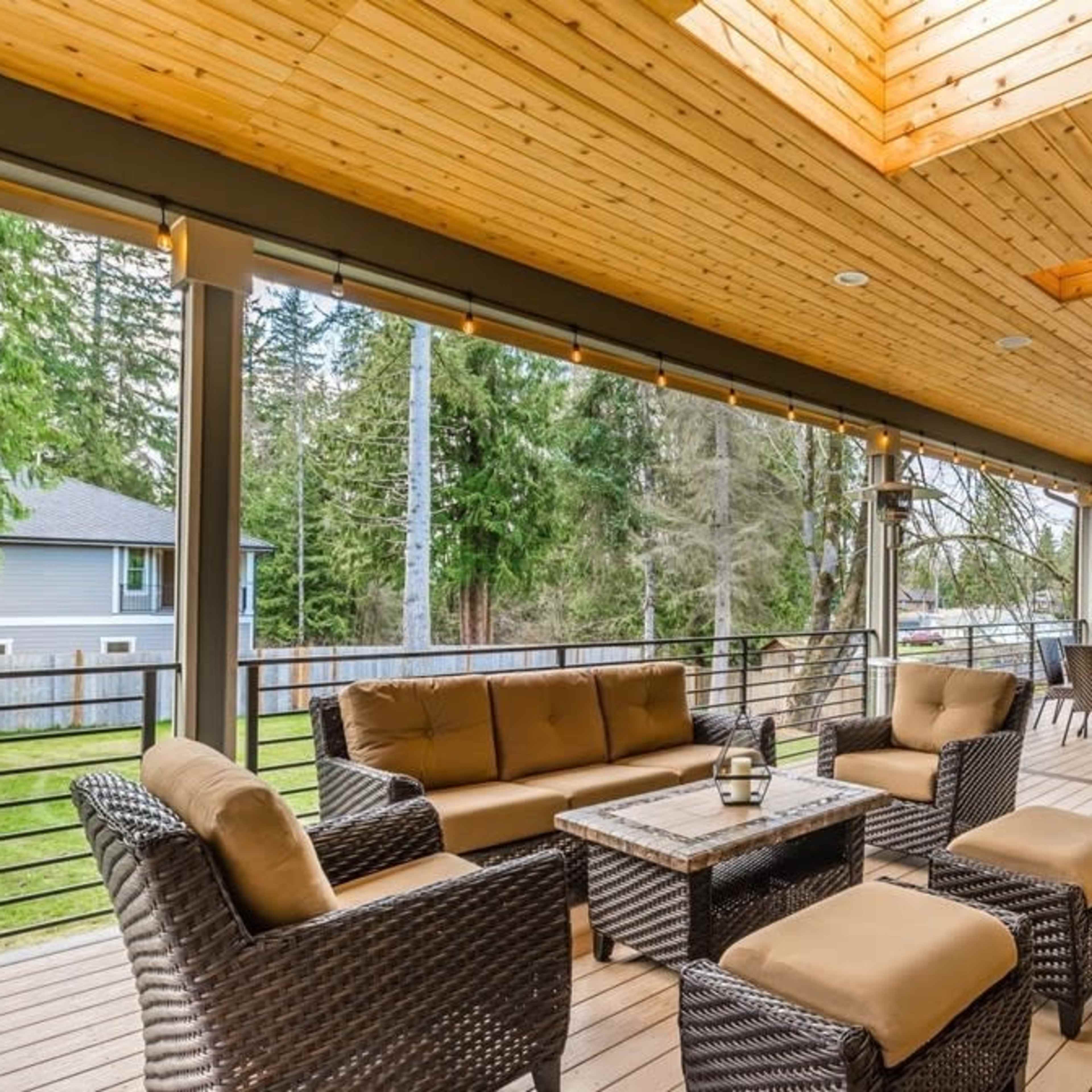 A spacious outdoor deck with wooden flooring, a sloped wooden ceiling, and a seating area consisting of wicker furniture and a table.