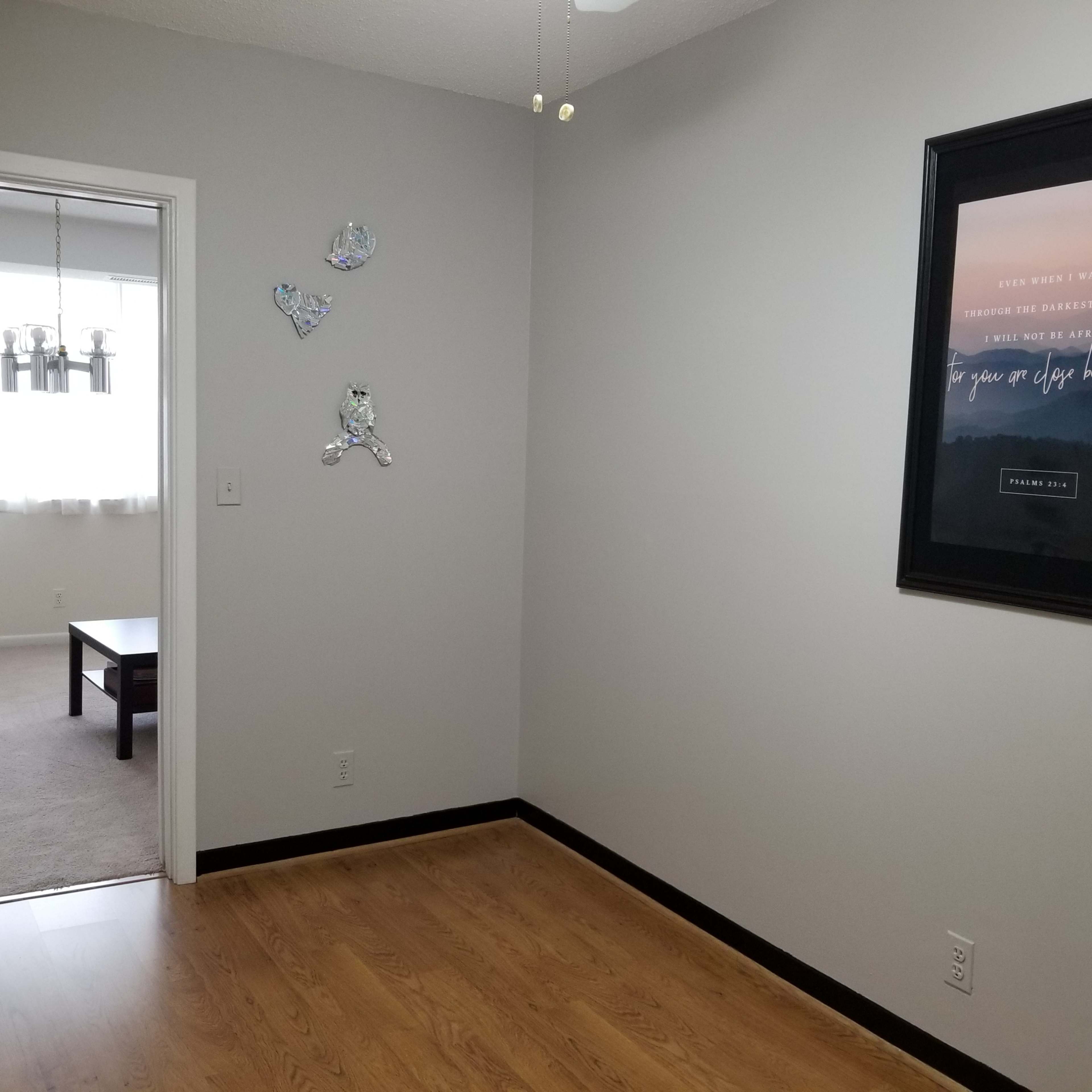 A clean kitchen area features a refrigerator, an adjoining living space visible through an open doorway, and a framed motivational poster on the wall.