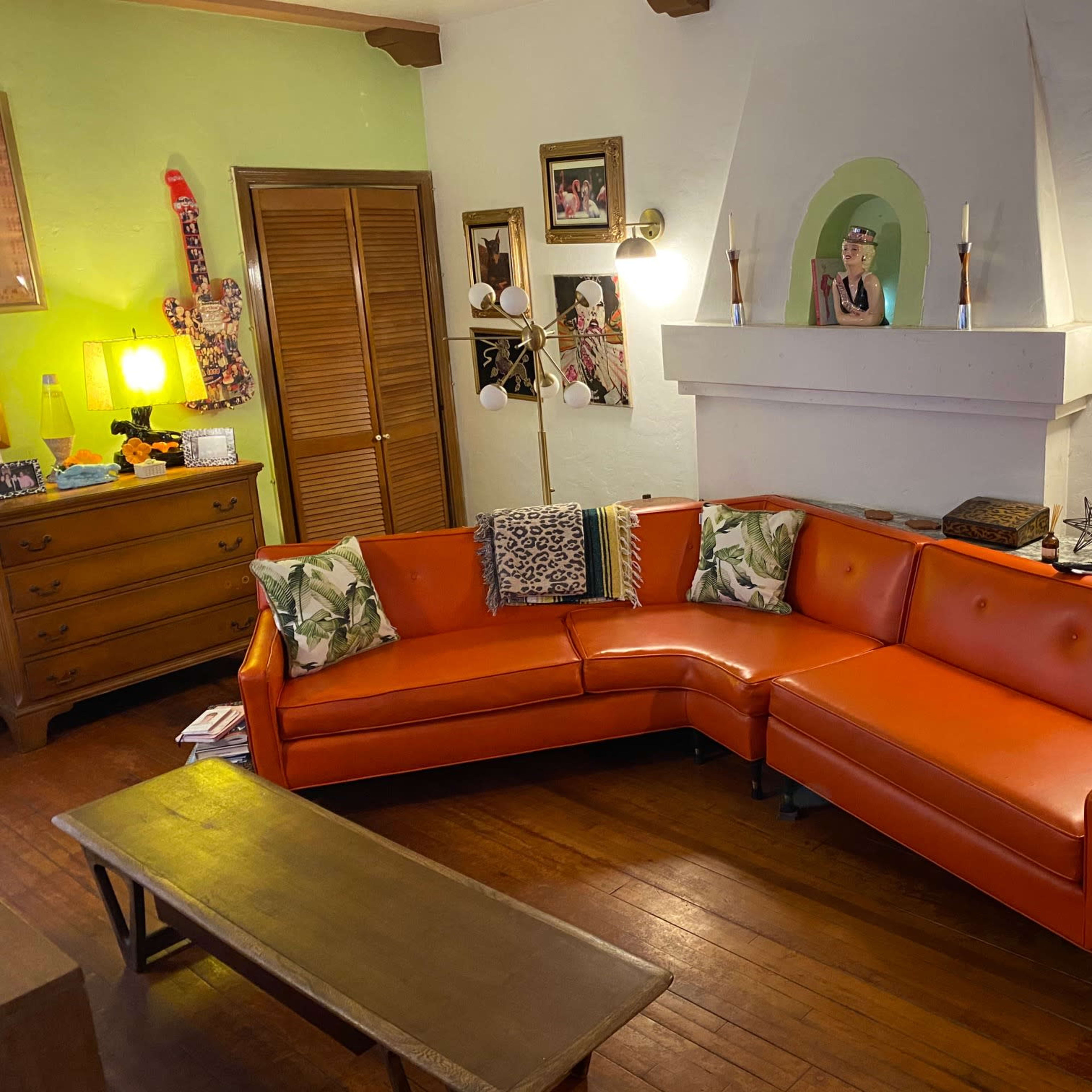 A cozy living room featuring an orange sectional sofa, wooden furniture, and a decorative fireplace surrounded by framed pictures.