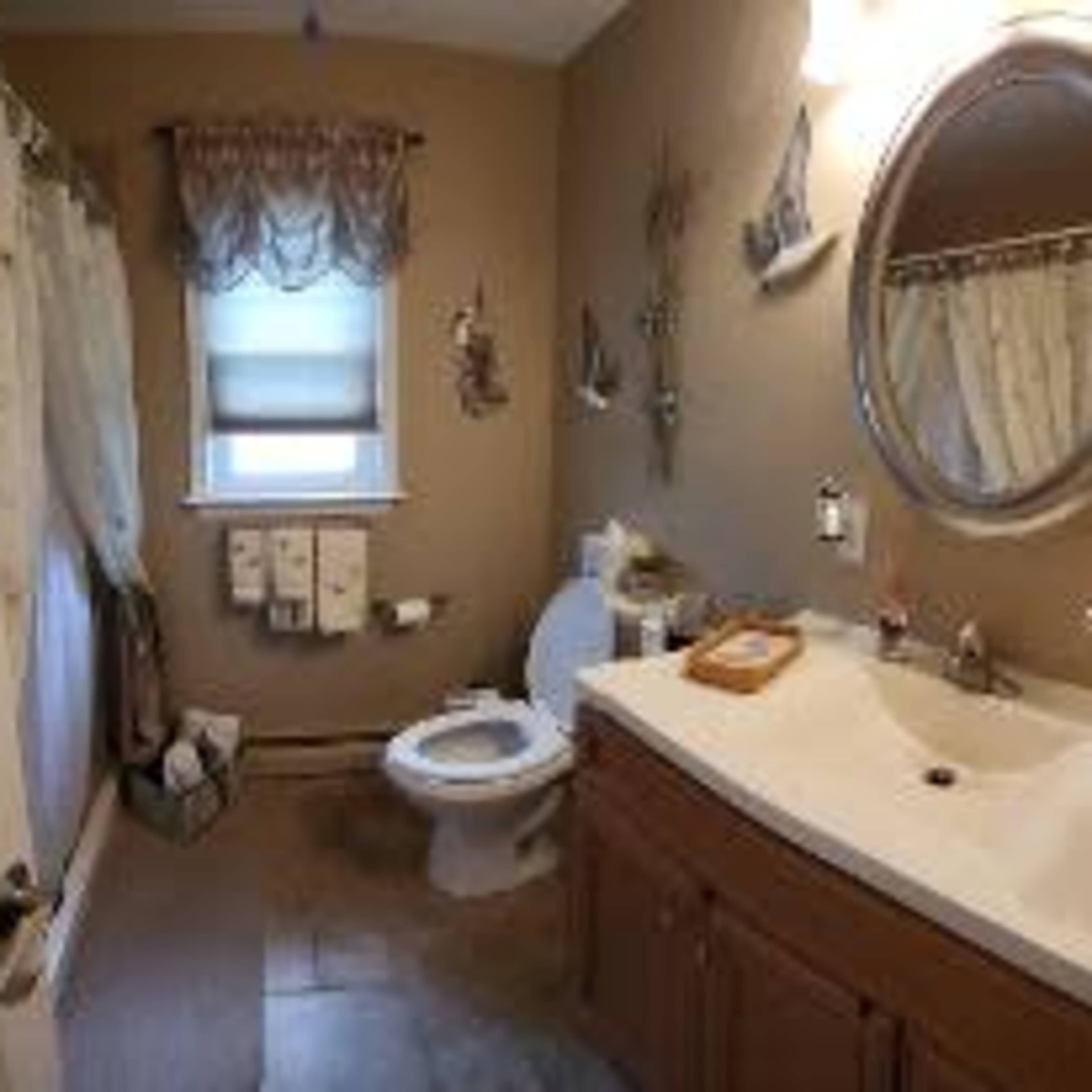 A clean bathroom features a toilet, a sink with a mirror, and towels arranged on the wall.