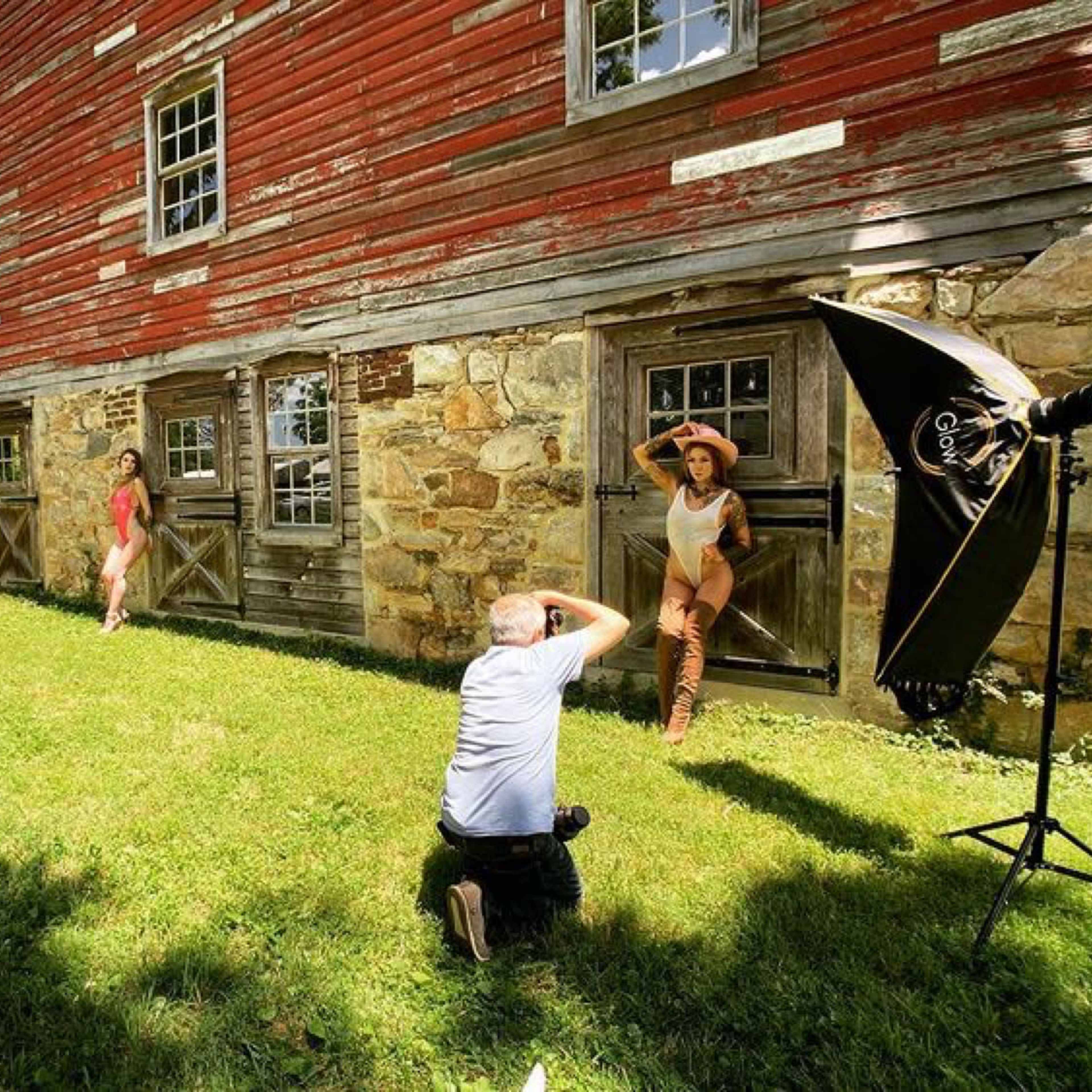 A photographer captures models posing in front of a rustic barn while an assistant sets up lighting equipment.