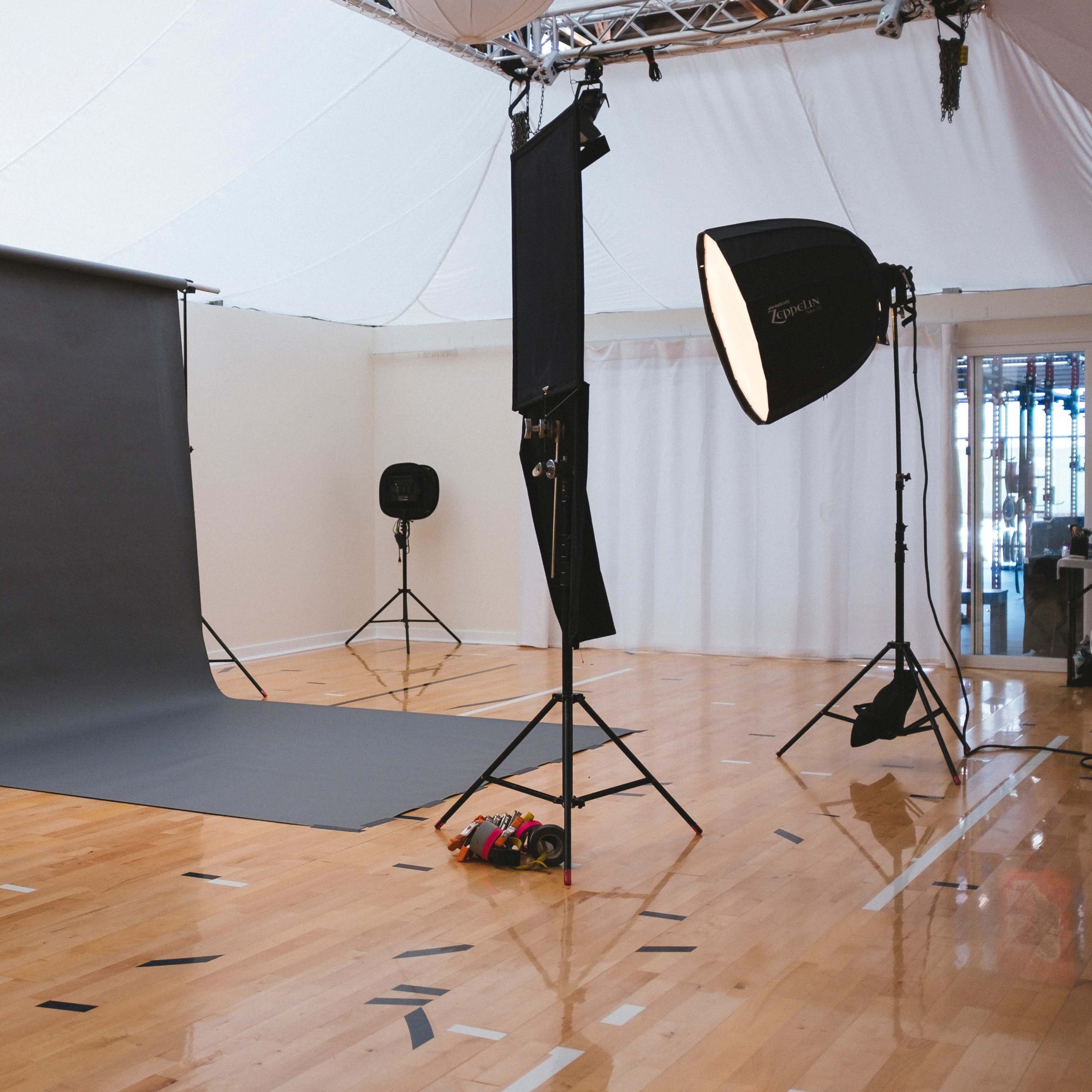 A photography studio with a gray backdrop, softbox lights, and a polished wooden floor.